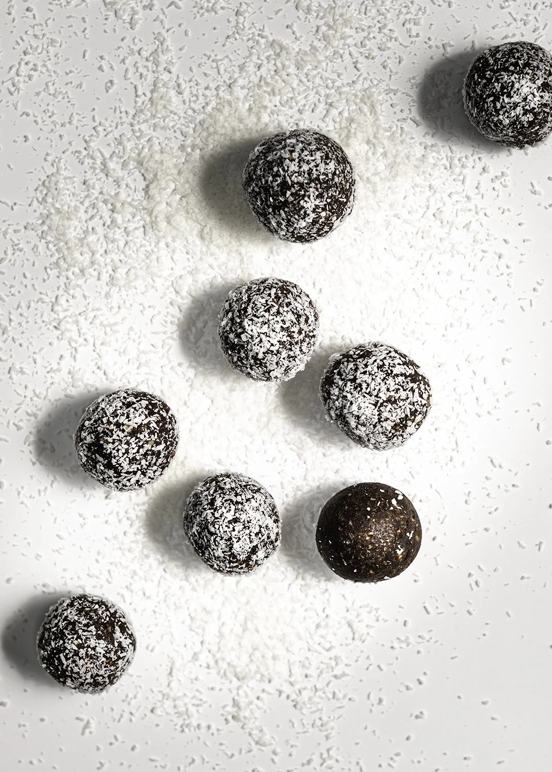 Chocolate balls coated with shredded coconut, scattered on a white surface with additional shredded coconut around them.
