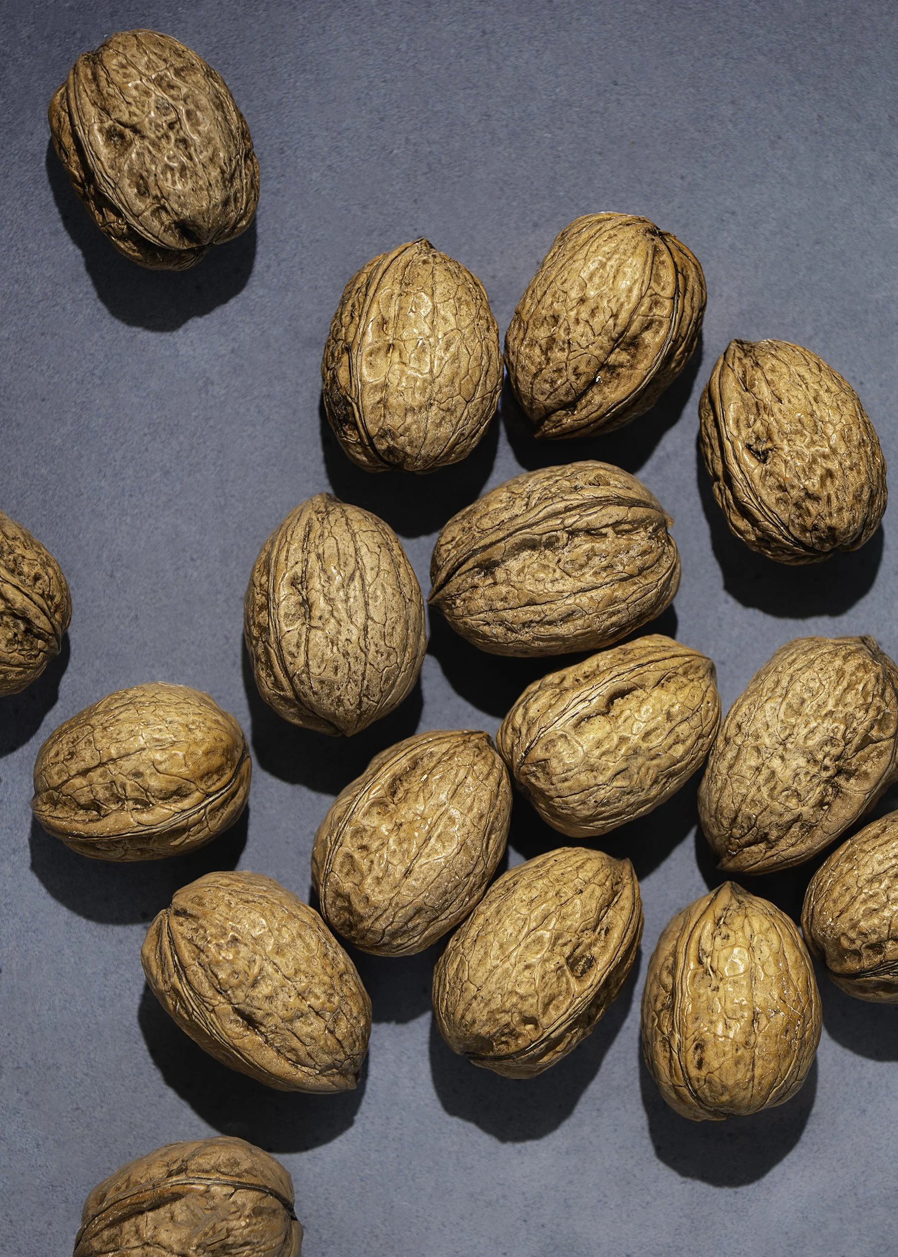 A collection of whole walnuts arranged on a flat surface with a light blue background, casting small shadows.