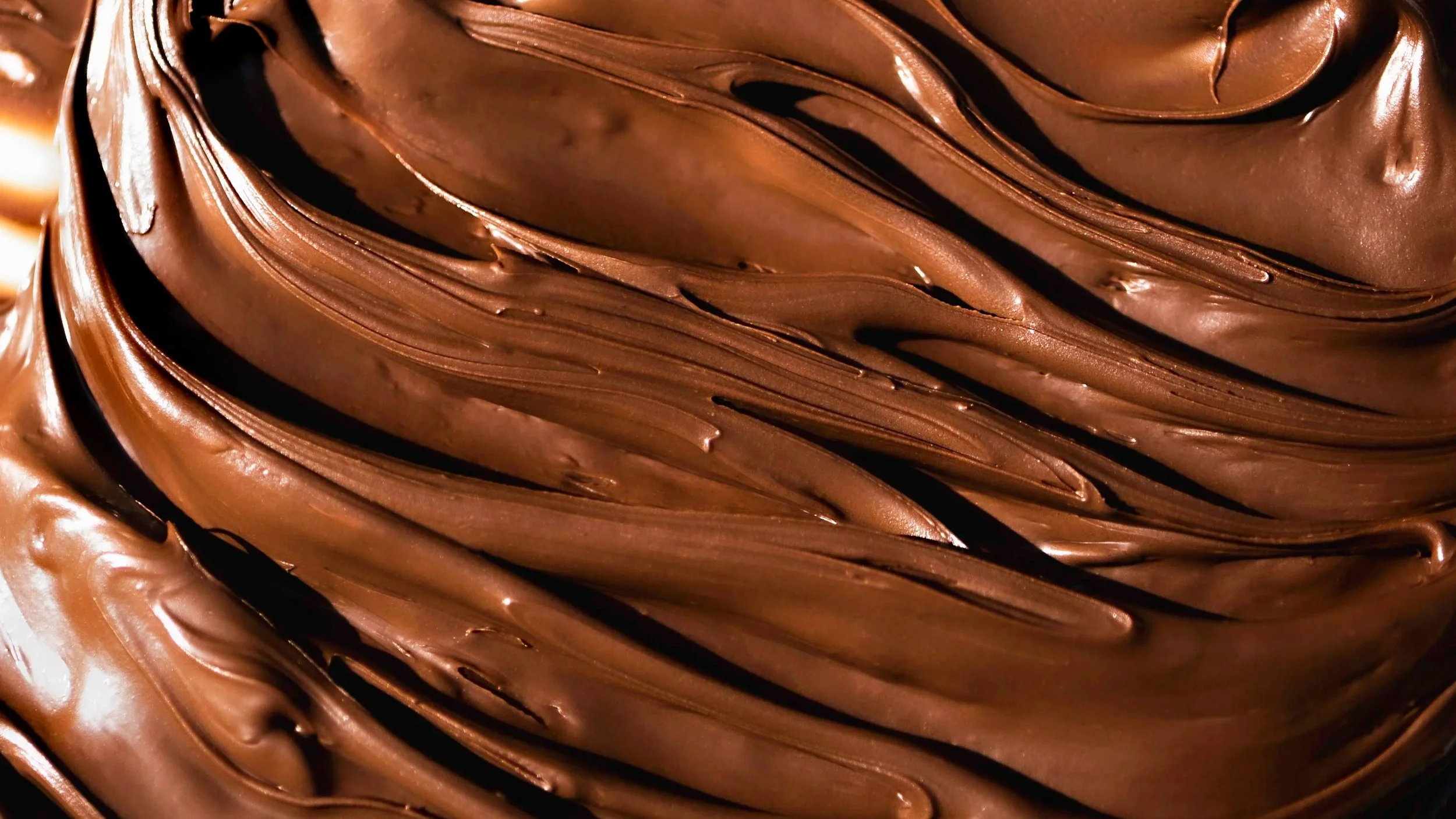 Close-up of rich, creamy, melted chocolate spread with smooth, glossy texture and swirls.