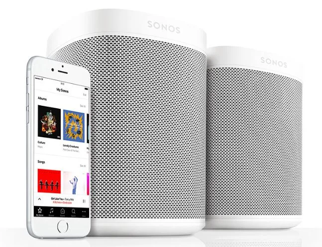Two Sonos speakers beside an iPhone running the Sonos app