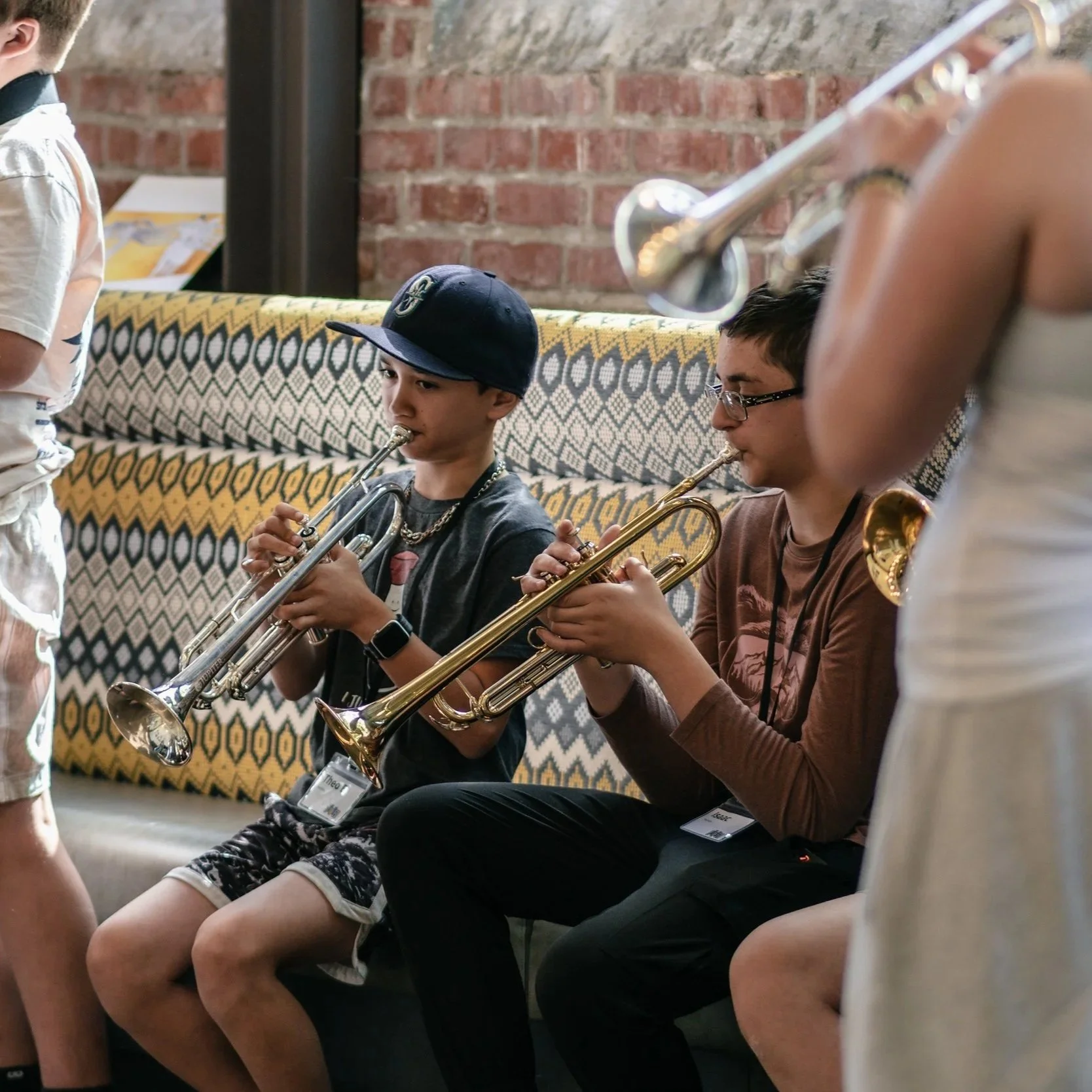 Two young students playing their trumpets while sitting down during break.