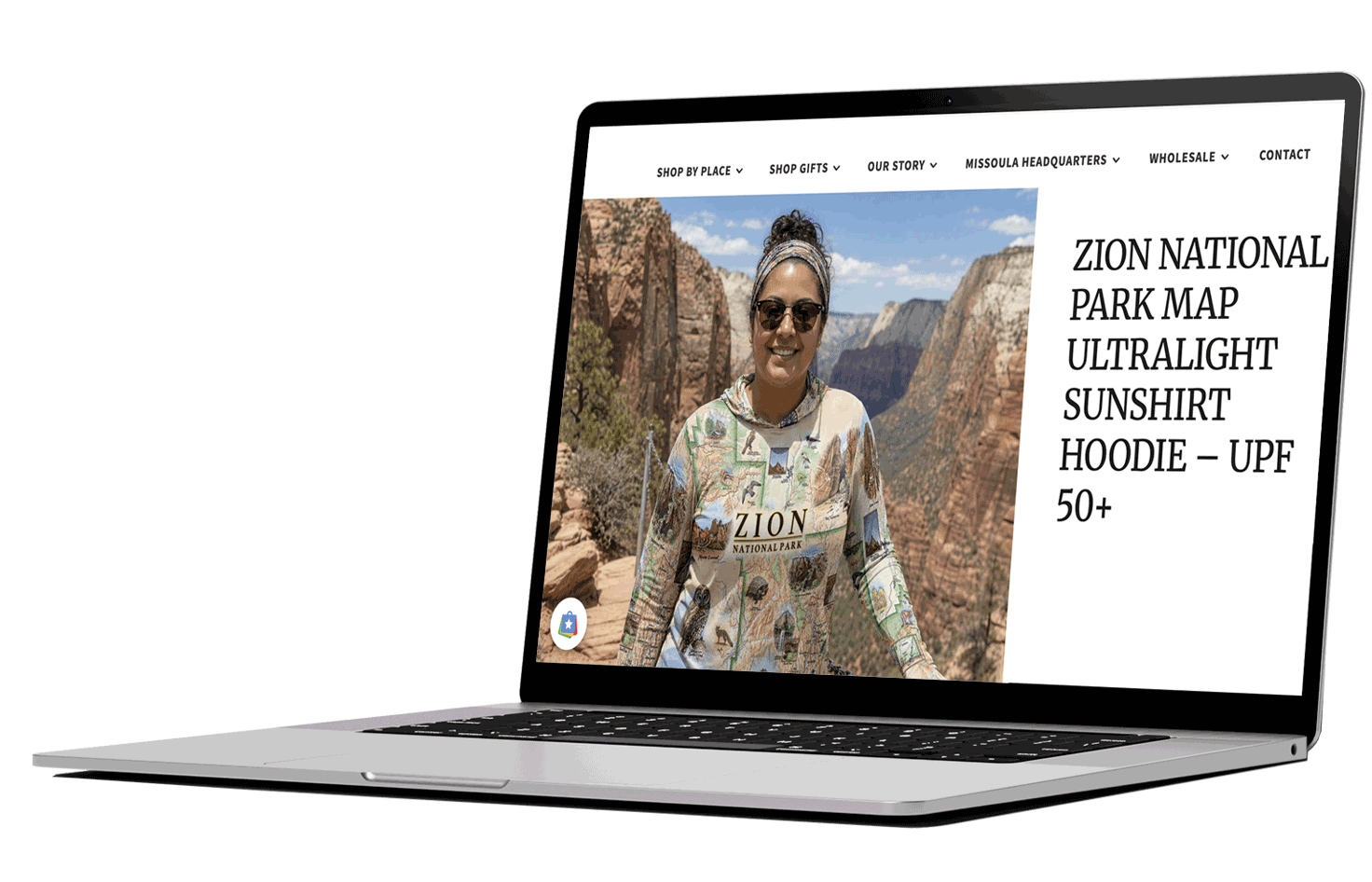 Laptop displaying a website with a photo of a woman in Zion National Park wearing a hoodie with the park map design, with canyon cliffs in the background.