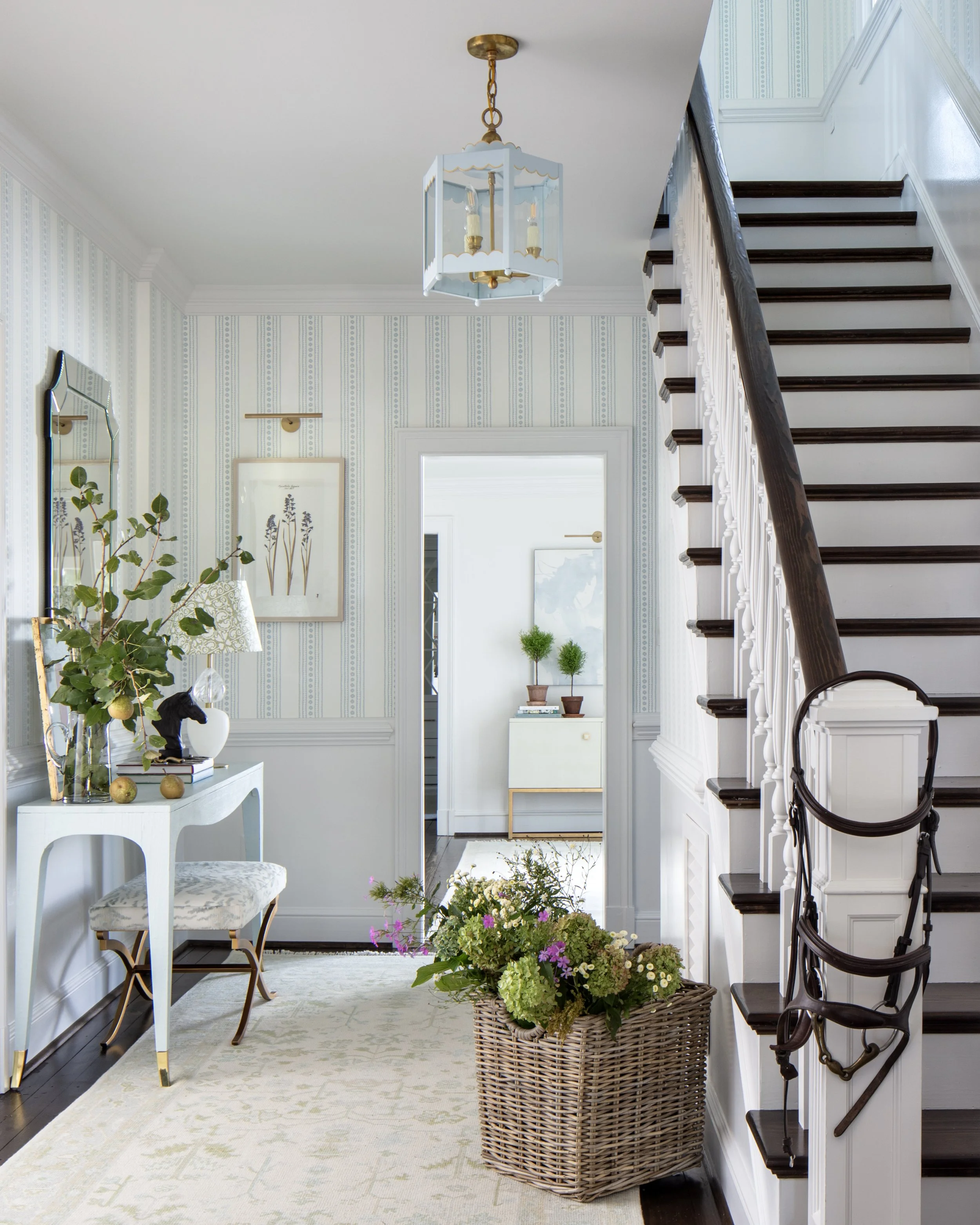 Elegant home entryway designed by Sara Hillery Interior Design in Richmond, VA, featuring a light blue lantern pendant, striped wallpaper, a white console table with greenery, and a classic staircase.