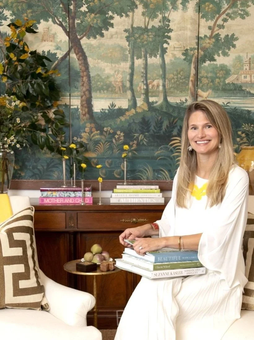 Award-winning Richmond interior designer Sara Hillery smiling in a room featuring green scenic mural wallpaper, a dark wood antique dresser, and custom-styled decor.