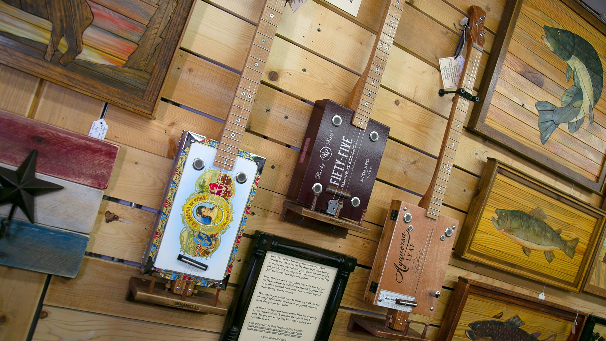 A variety of cigar box guitars are displayed on a wall.