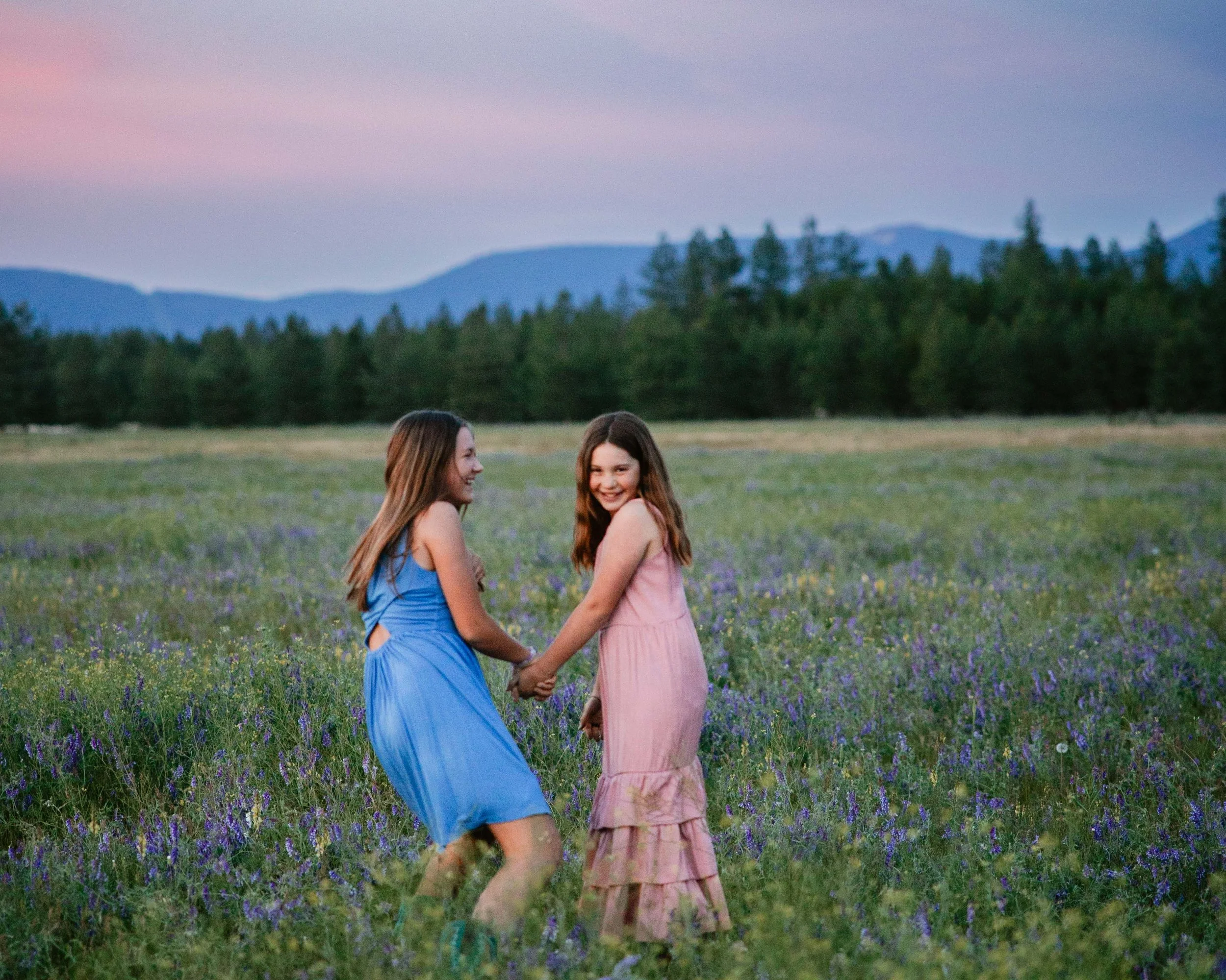 Sisters running in field of wildflowers at sunset in Athol, Idaho