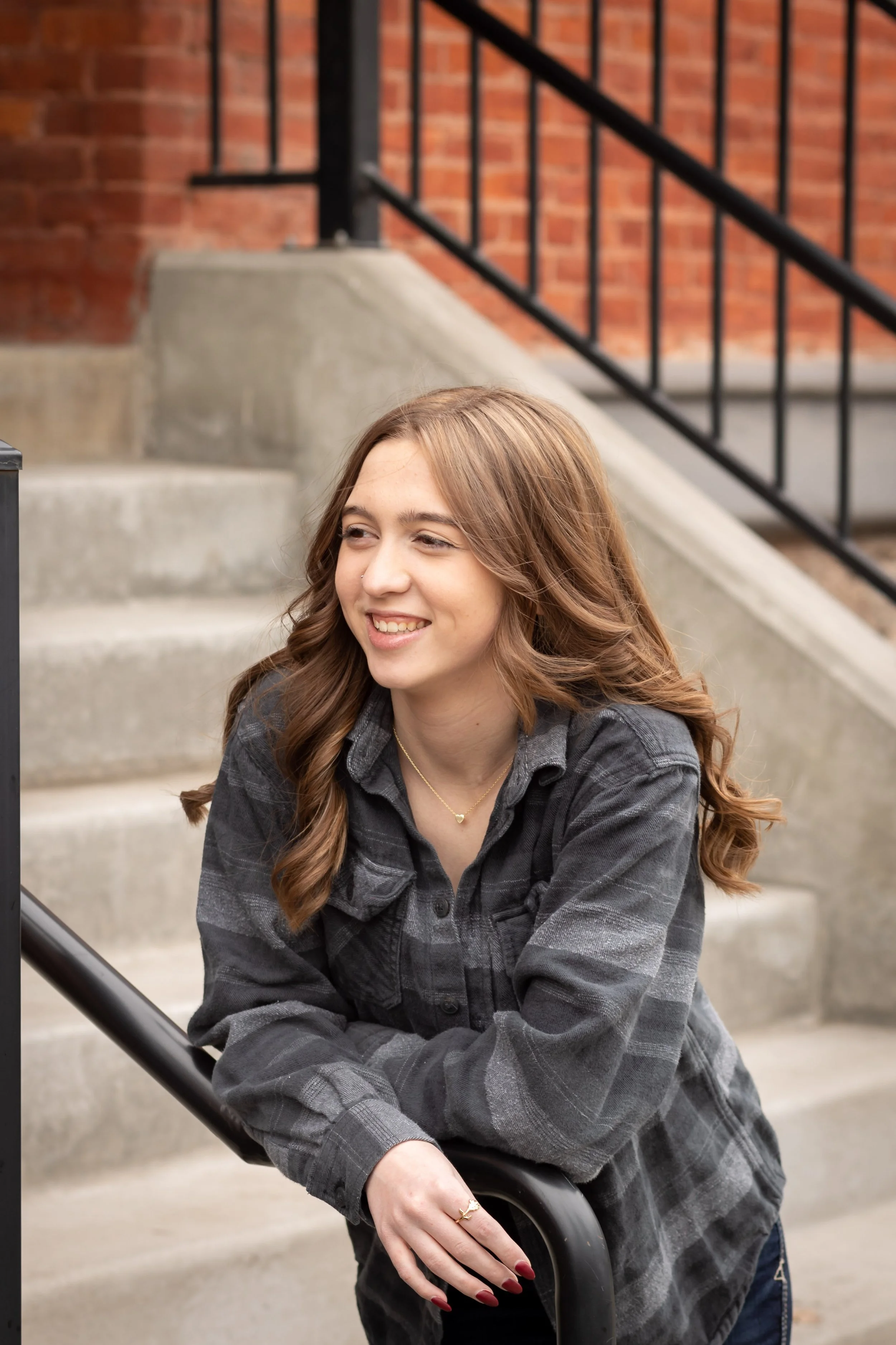 High school senior leaning on a stair railing during an urban senior photo session in downtown North Idaho wearing a casual flannel outfit.