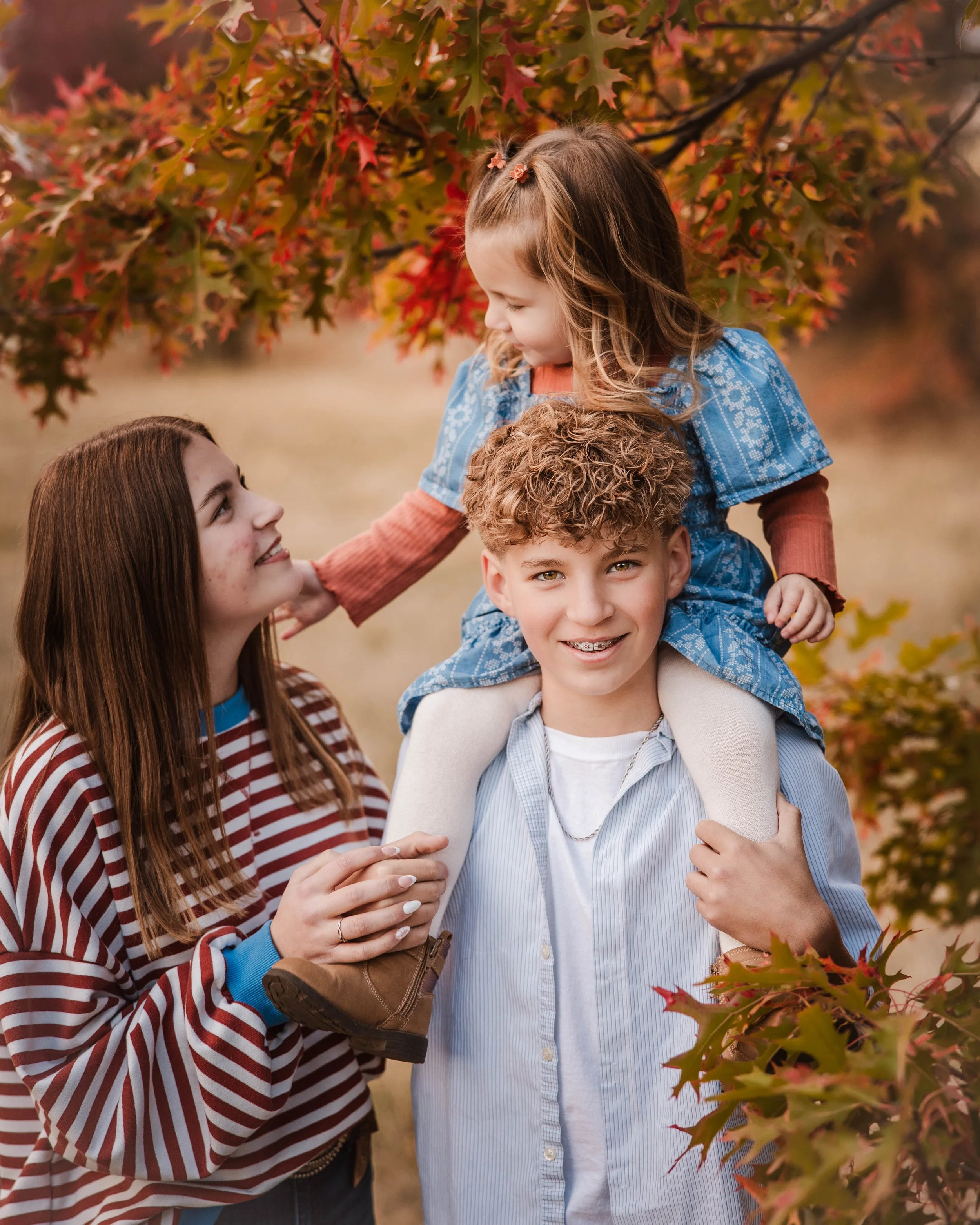 Three siblings laughing and playing together under colorful fall leaves during a relaxed family photo session in North Idaho.