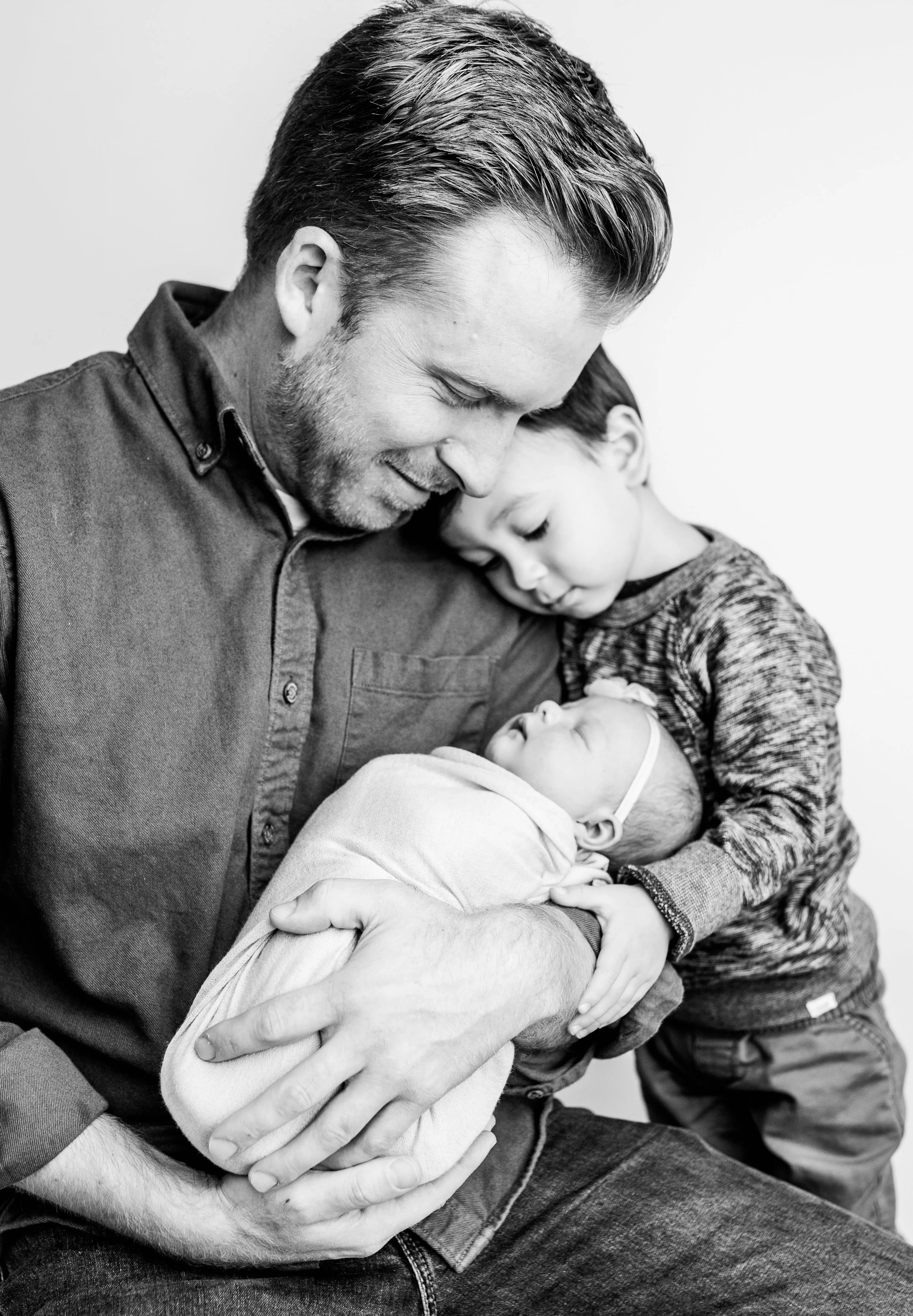 father son and newborn baby girl in loving embrace admiring new sister black and white