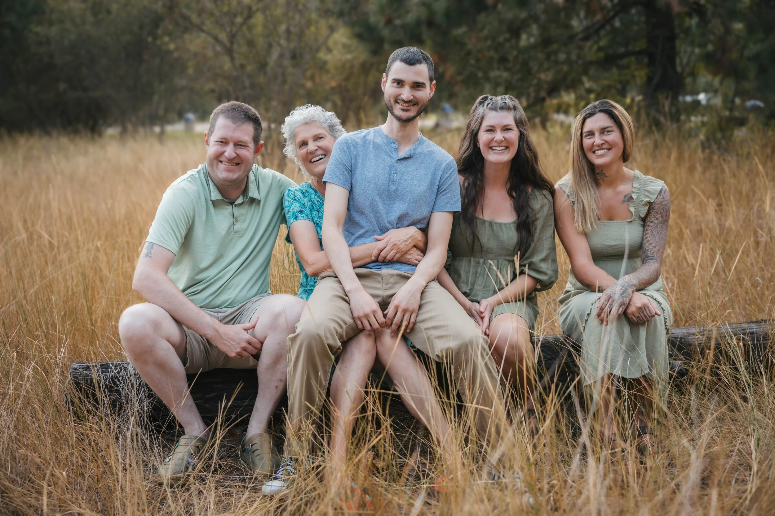Extended family sitting together in a golden field during an outdoor family photo session in North Idaho with natural scenery and warm evening light.