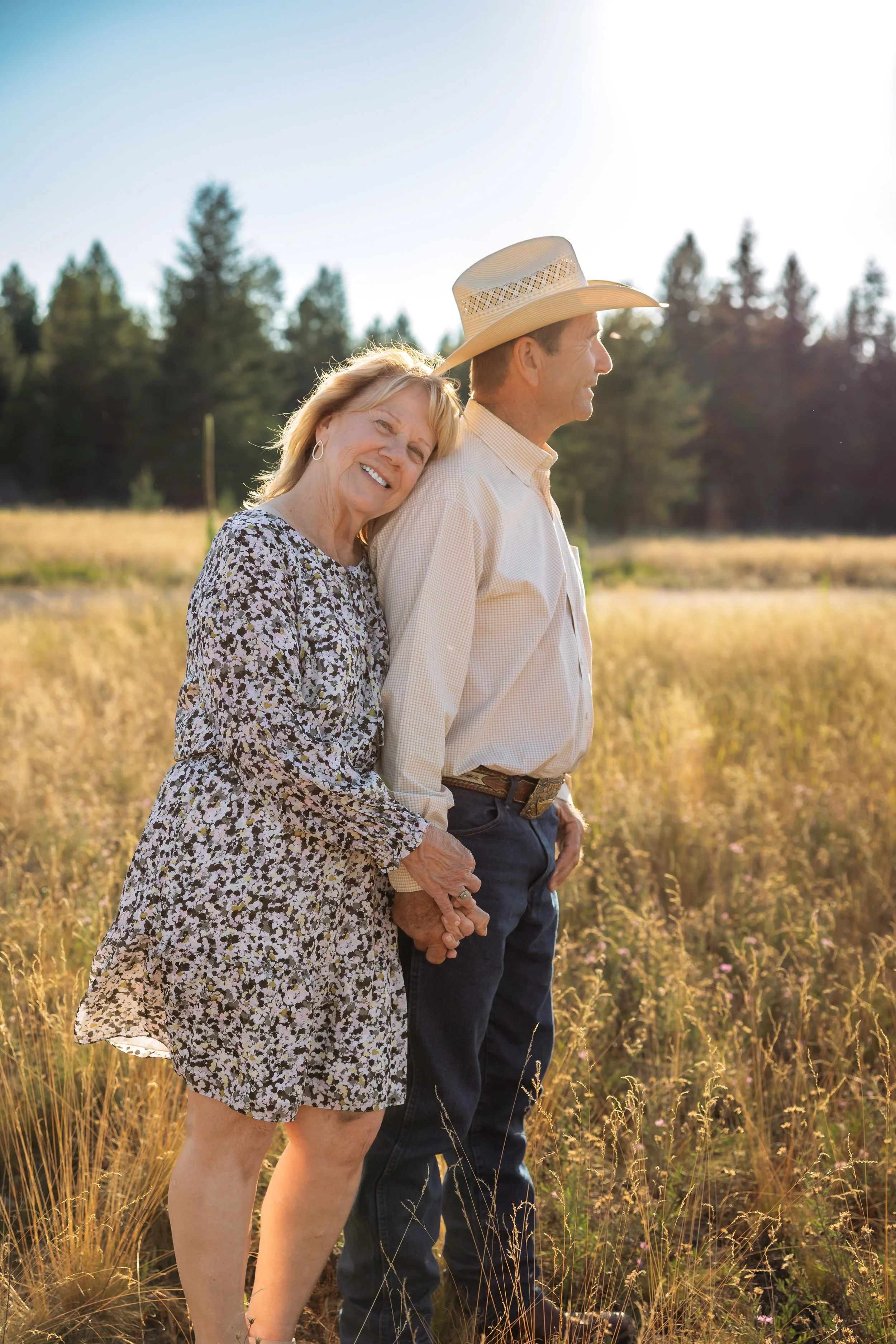 Couple standing together in a sunlit meadow during a golden hour family photo session in North Idaho with pine trees in the background.