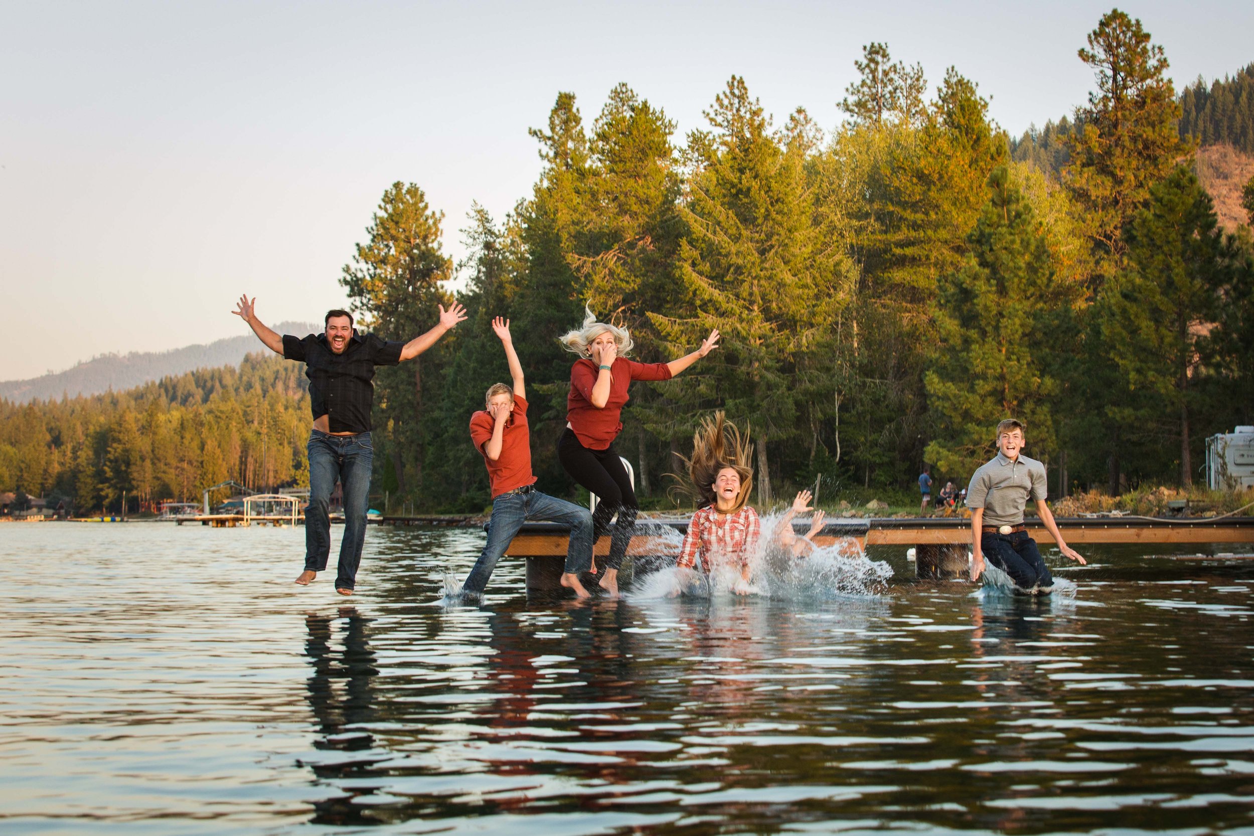 Family photography session in North Idaho with family jumping into lake capturing candid playful moment