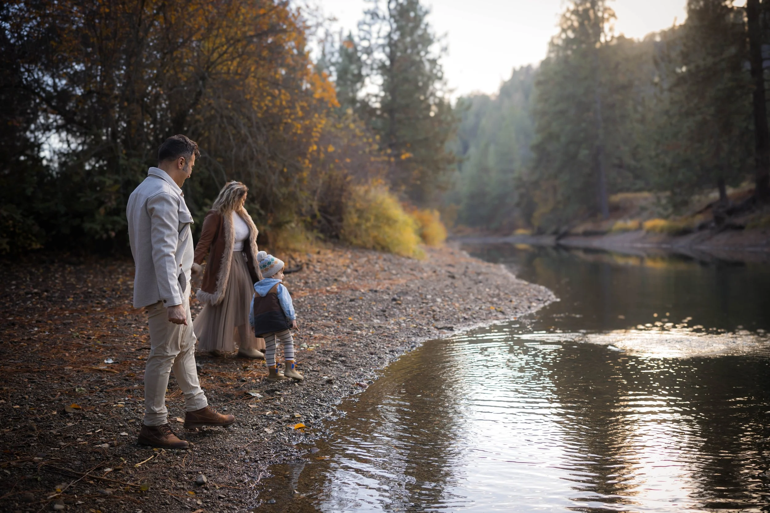 Family laughing and twirling together beside the water during a fall portrait session in North Idaho.