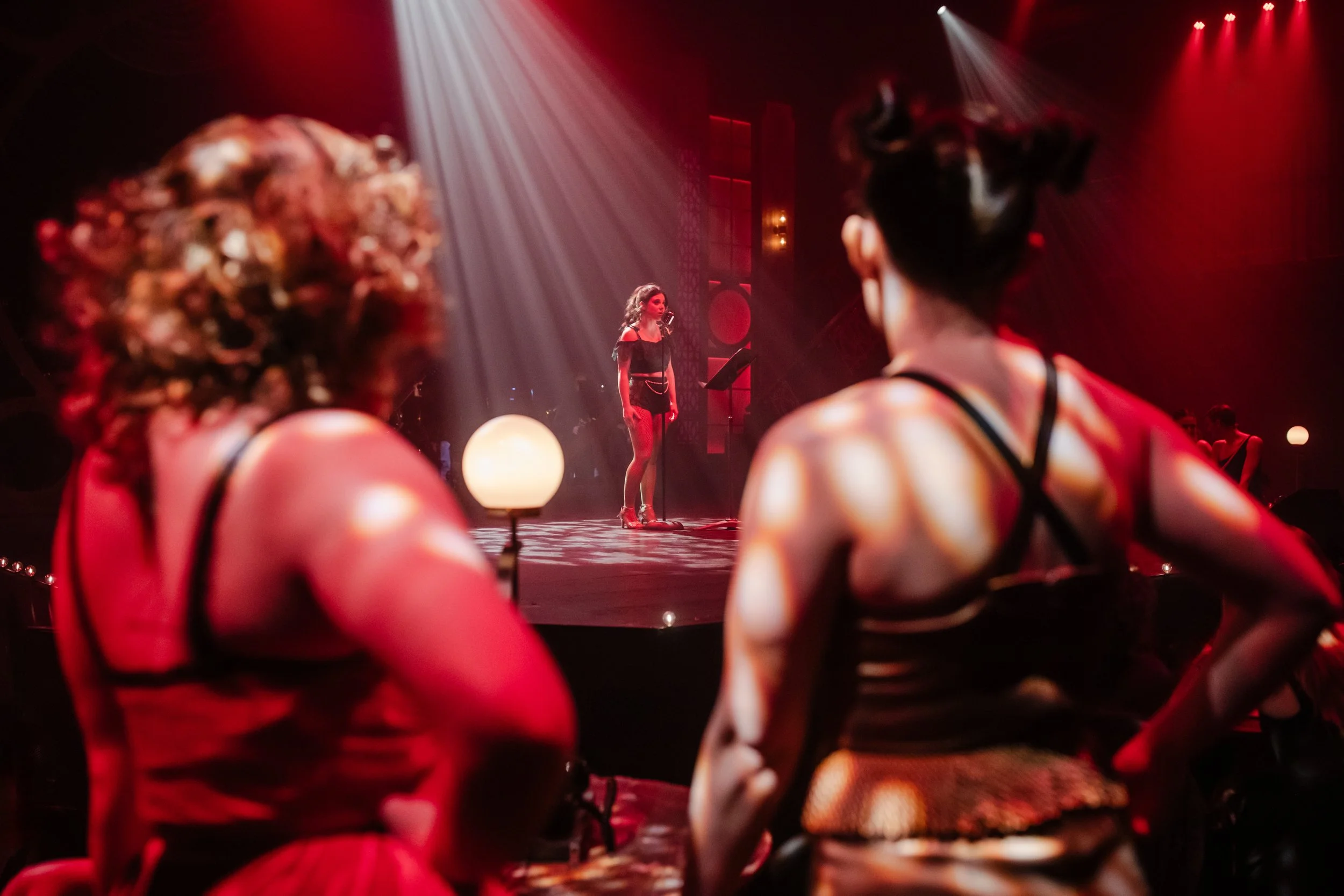 Immersive Cabaret theatre set design featuring a raised central stage, visible onstage band, multi-level platforms, and club-style audience seating surrounding the performance space, designed by Creativesphere.