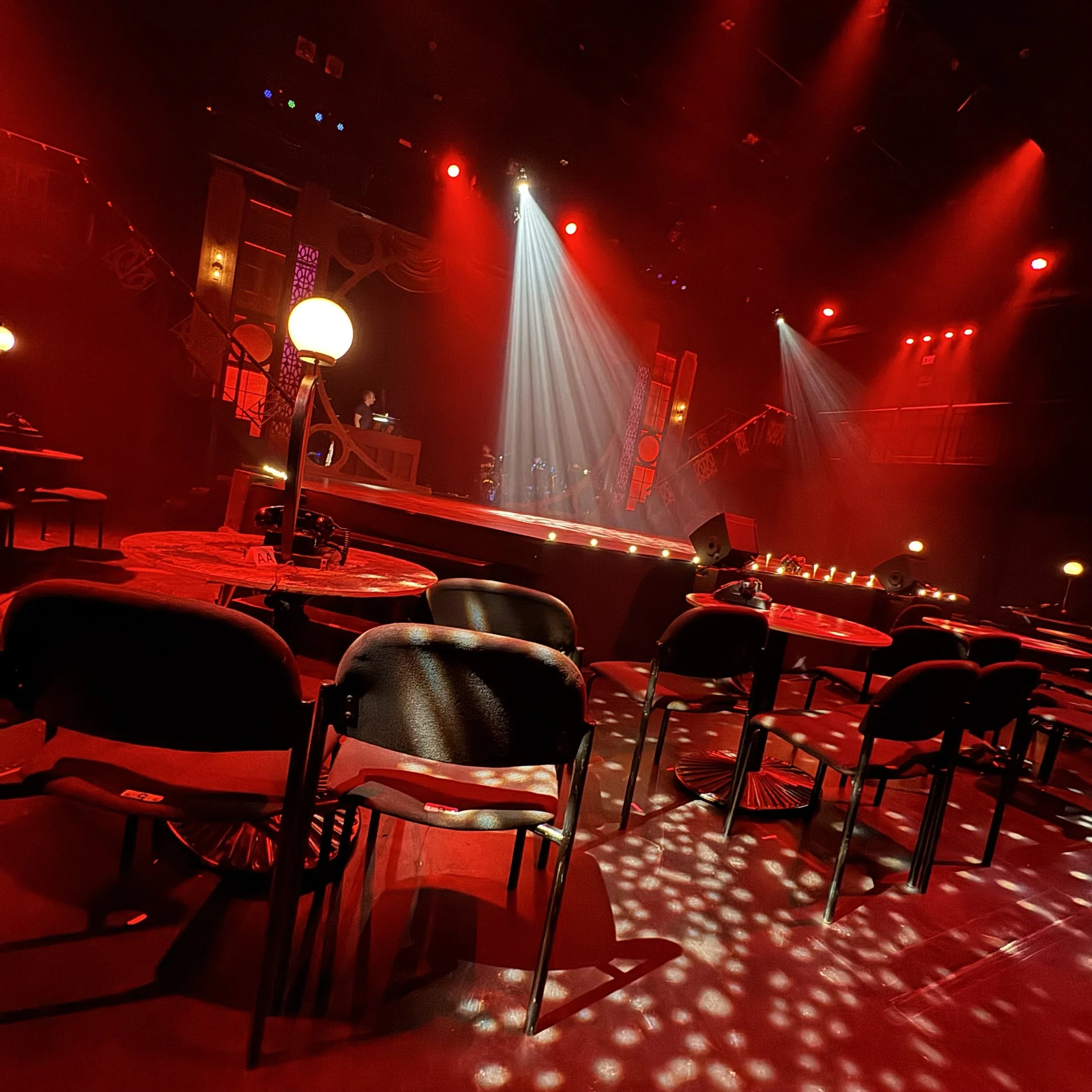 Immersive Cabaret theatre set design featuring a raised central stage, visible onstage band, multi-level platforms, and club-style audience seating surrounding the performance space, designed by Creativesphere.