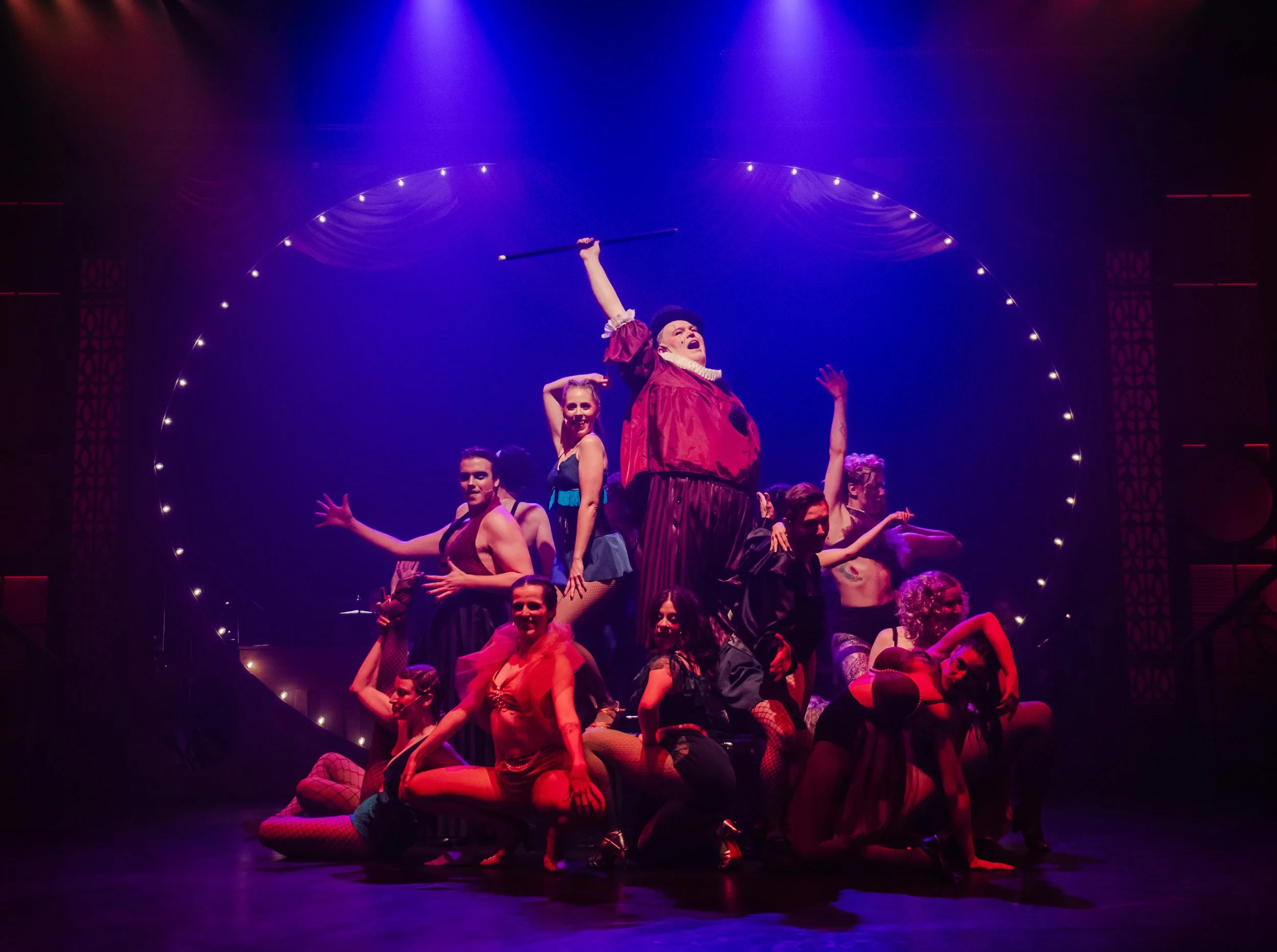 Immersive Cabaret theatre set design featuring a raised central stage, visible onstage band, multi-level platforms, and club-style audience seating surrounding the performance space, designed by Creativesphere.