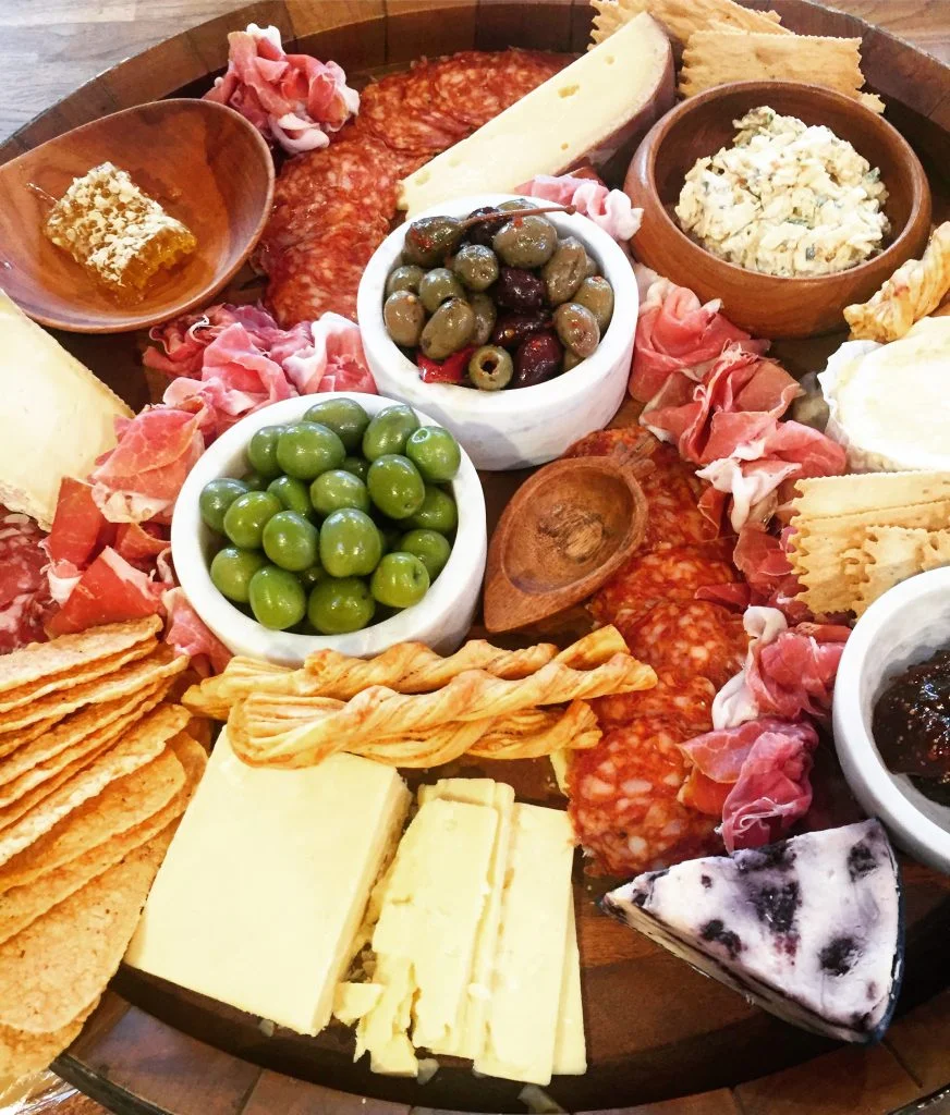 Then its all about layering! Add in rows of salami or make little bunches of prosciutto for a pretty floral look. Then add in crackers and jam into bowls. Its about variety in ingredients and color that makes a platter like this pop!