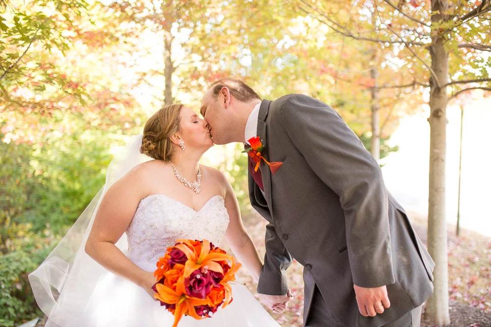Bride and groom kissing under the fall leaves during their October wedding at the Westin Washington Dulles Hotel