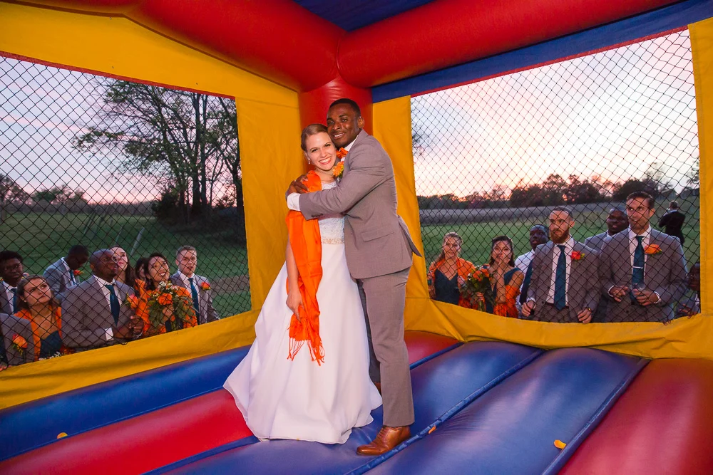 Bride and groom in the moon bounce while bridal party looks on