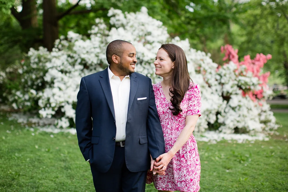 Happy engaged couple in front of white flowering bush in Central Park | Candid engagement photos in NYC