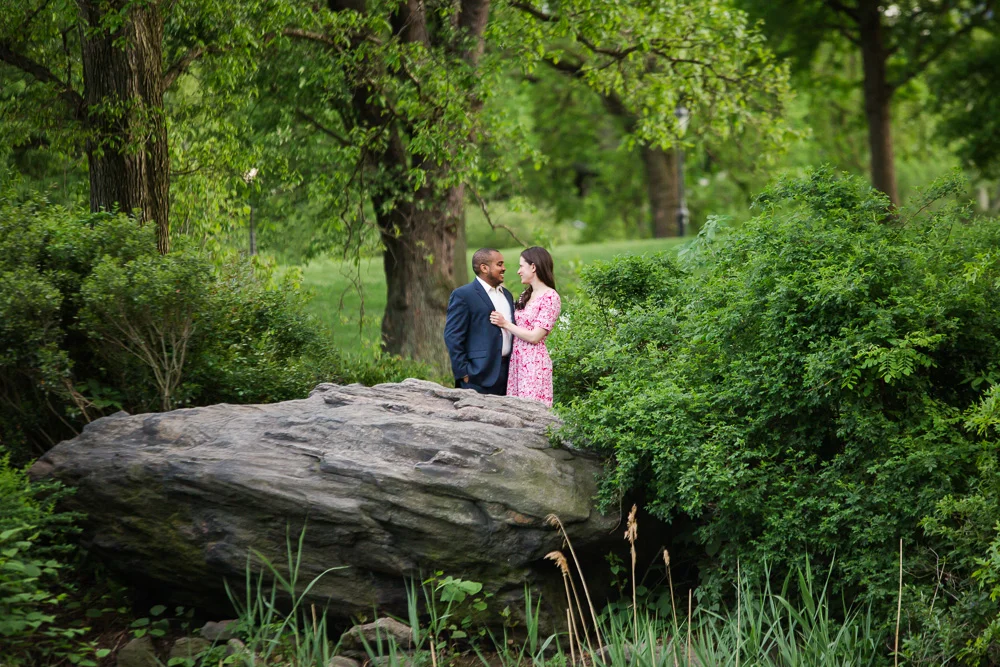 Engaged couple on the rocks near the Bow Bridge of Central Park | Best Central Park Engagement Photo Locations