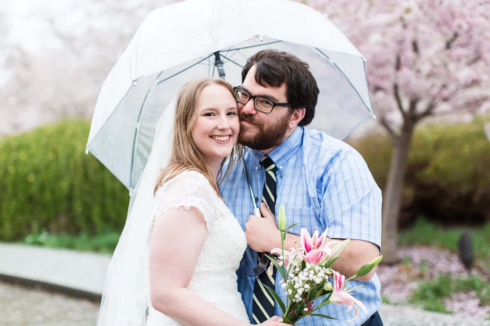 Wedding couple cuddles under an umbrella on their rainy DC wedding day