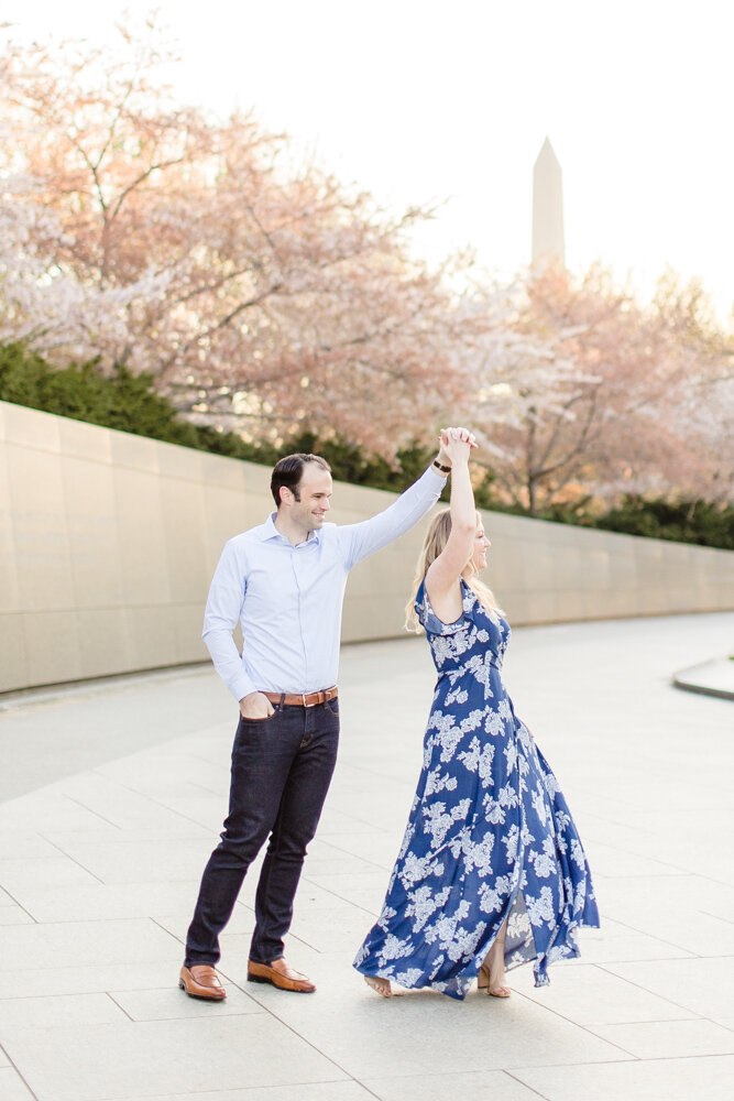 Engaged couple dancing by the cherry blossoms and Washington Monument