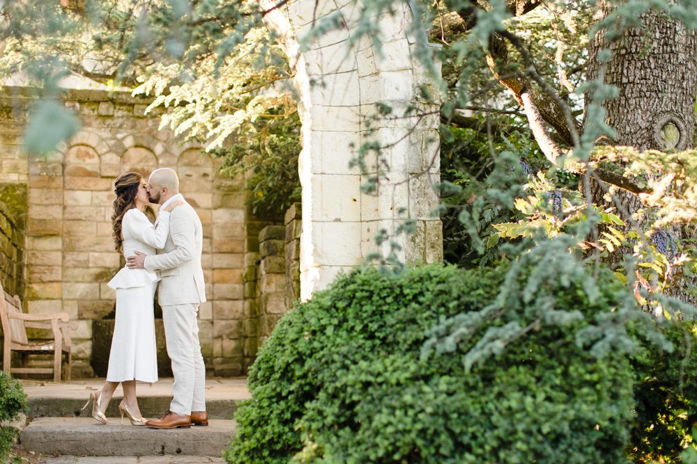  Wedding couple kiss under a stone arch in the Bishop’s Garden at the National Cathedral 