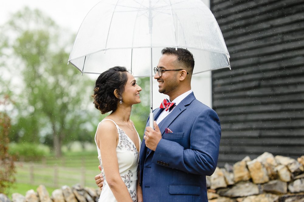 Bride and groom smiling under a clear umbrella