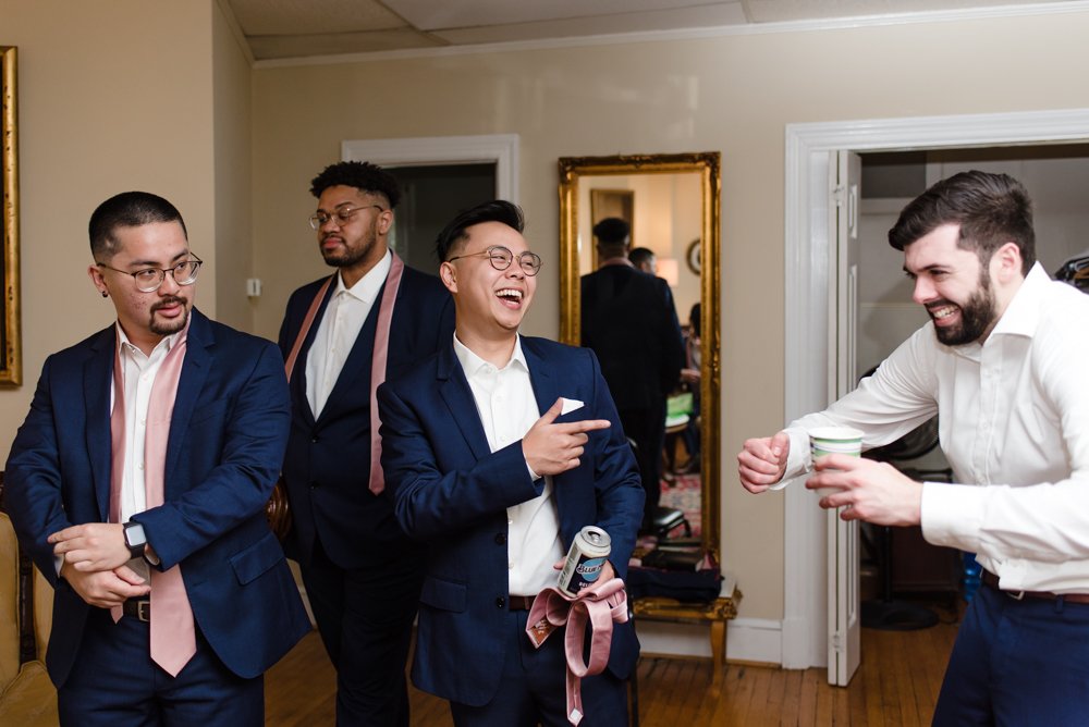 Groom laughing with groomsmen while getting read