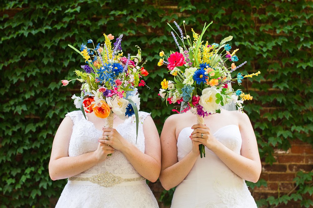 Two brides holding bouquets over their faces