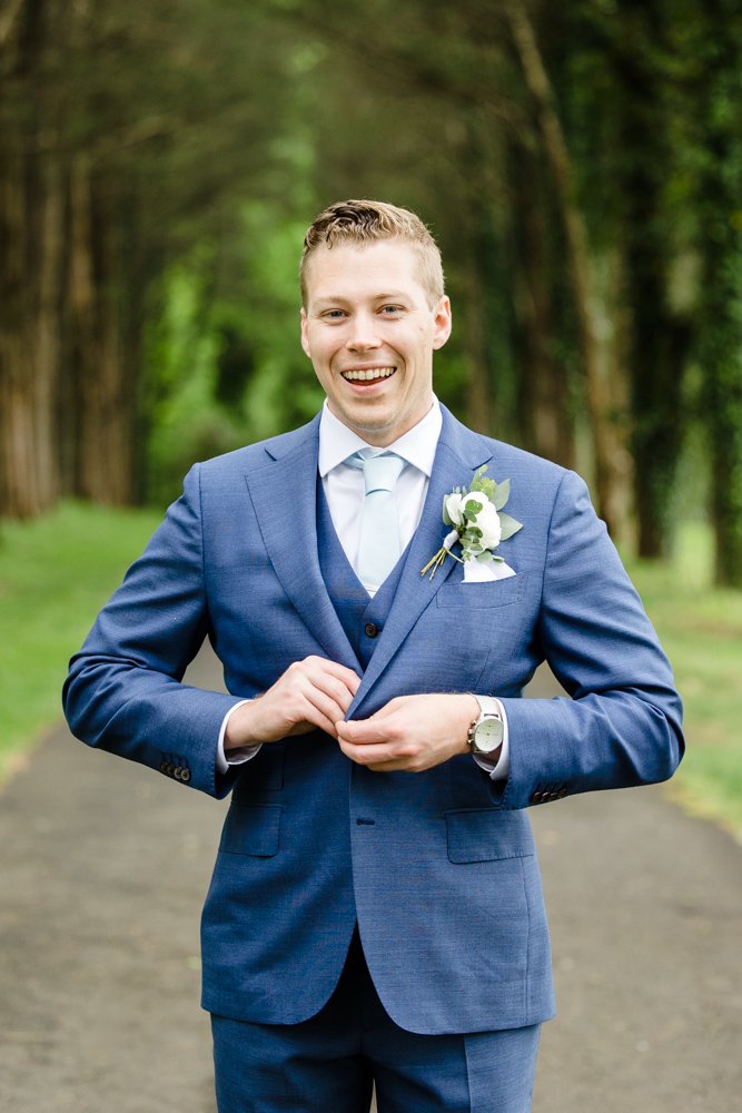  Groom smiling as he buttons up his suit jacket 