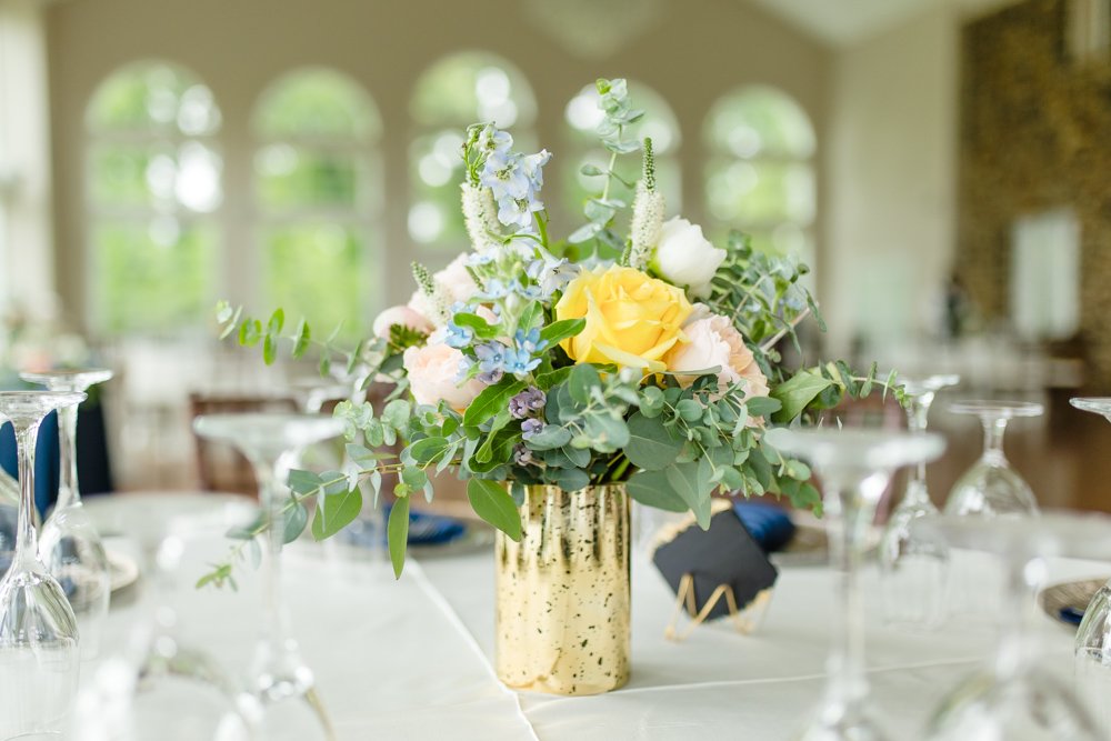  Centerpiece with yellow, peach, and blue flowers in a gold vase 