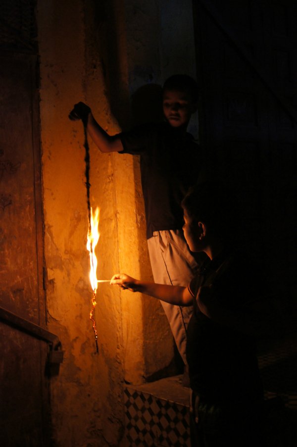 Two boys play with fire after dark, in the streets of Mekenes' old city. Meknes, Morocco - 2011.