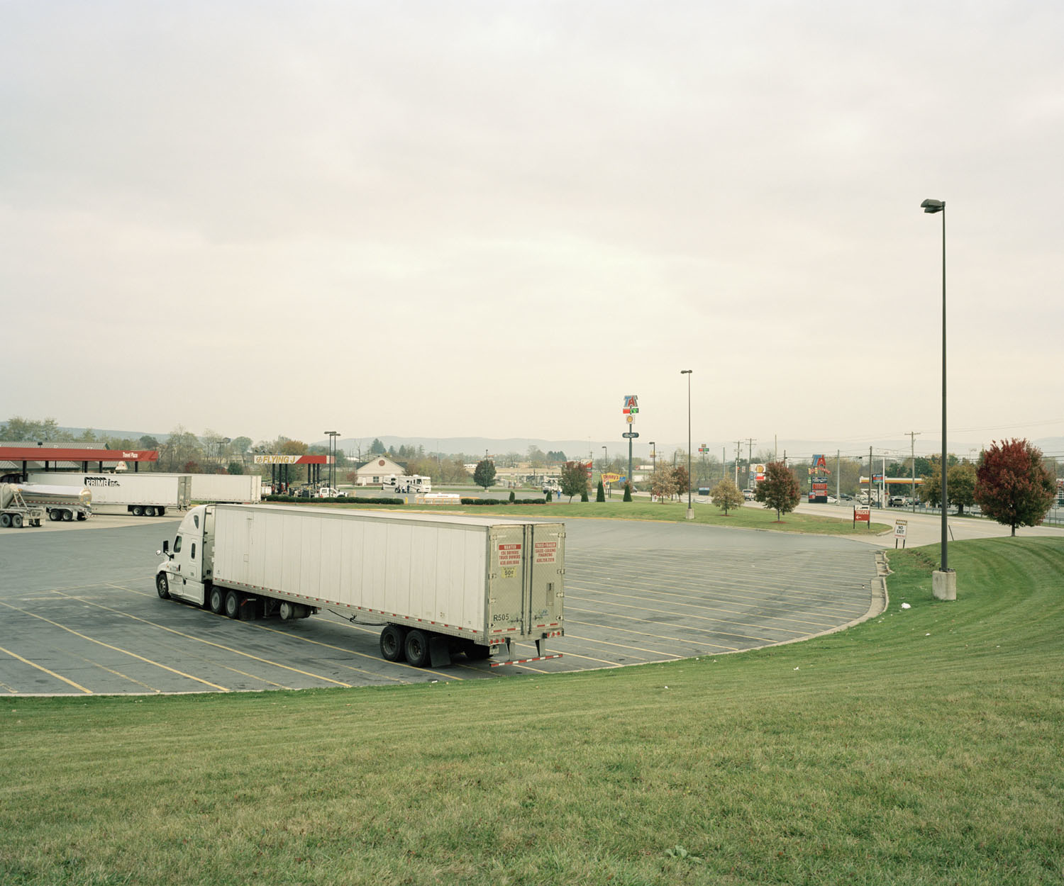 The Straightest Path Allowed by Law is a new photographic work, forming a topographic exploration into the relationship between high-frequency trading routes and the phenomenon of the American landscape. In 2010, the Allegheny mountain region of Pennsylvania was drilled through to make way for a private fibre-optic cable line linking the major trading capitals of America – New York and Chicago. Largely conducted in secret, the $300 million project was constructed to speed up high-frequency trading times by a matter of milliseconds. Much of the route follows small paved roads, bridges and railroads due to laws against laying fibre on interstate highways, the challenge became constructing “the straightest path allowed by law”*. The Allegheny Mountains are often noted, if somewhat vaguely, in articles and academic writing on the subjects of high-frequency trading as being the toughest challenge for the private firm Spread Networks who commissioned the project, because of the hard limestone known as ‘blue rock’. In October 2014 I undertook a trip to the region, intrigued by what I would find there. Dotted in between pastoral landscapes of cornfields, local Amish communities, vast forests, national parks and small mountain towns are the occasional signifier of this vast project– a small white and orange poll. However, the line itself, being an inch and a half wide, does not hold particular significance in terms of its monumental impact on the environment. Rather, I am drawn to what this landscape represents as a topographic survey of economics, the incongruous relationship between the local and the global and the invisible presence of financial markets in a seemingly vernacular landscape. 2014 *Michael Lewis, Flash Boys