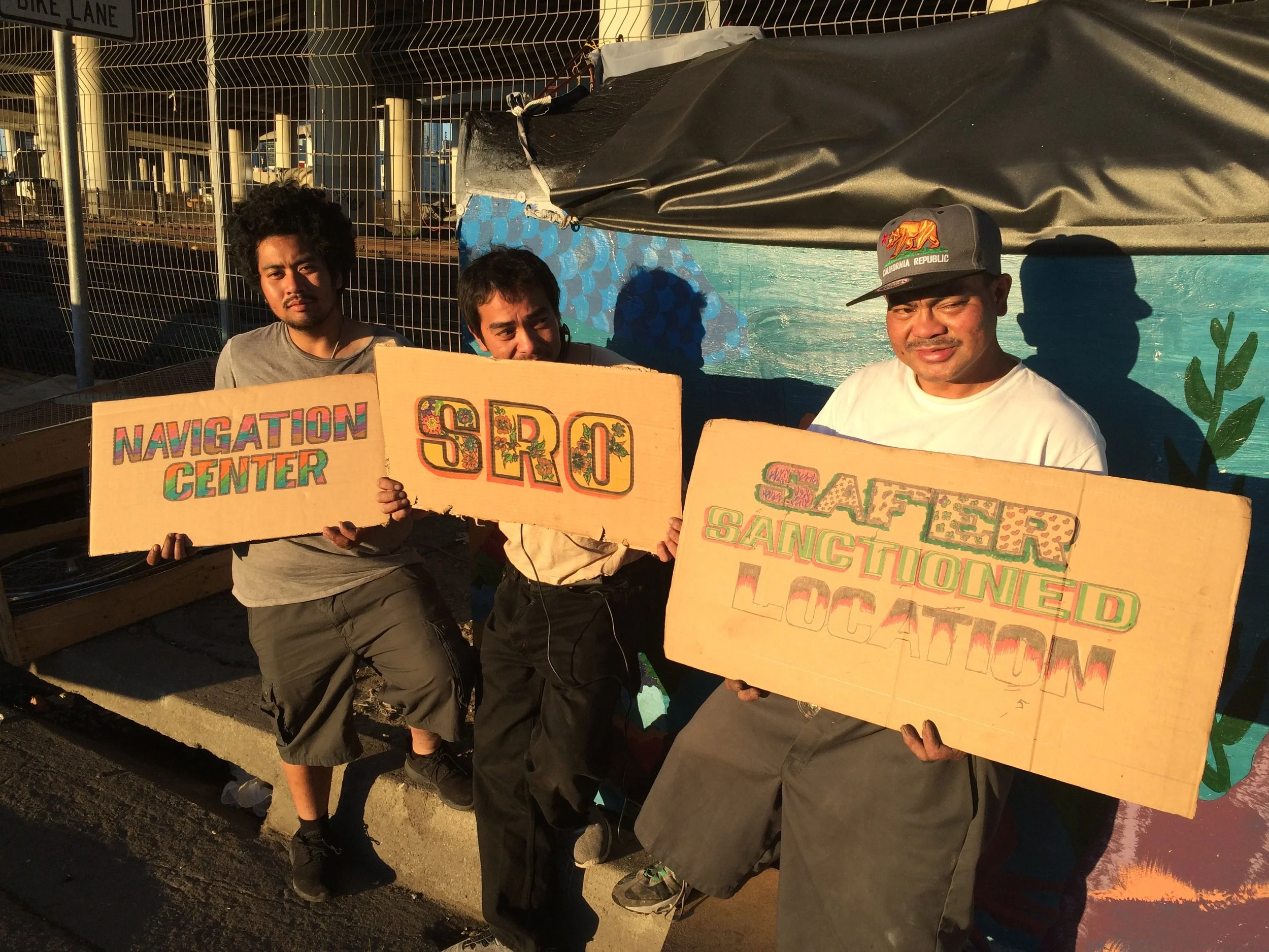 Box City encampment residents (7th Street at Mission Bay) holding up signs with transition goals (Fall 2016)