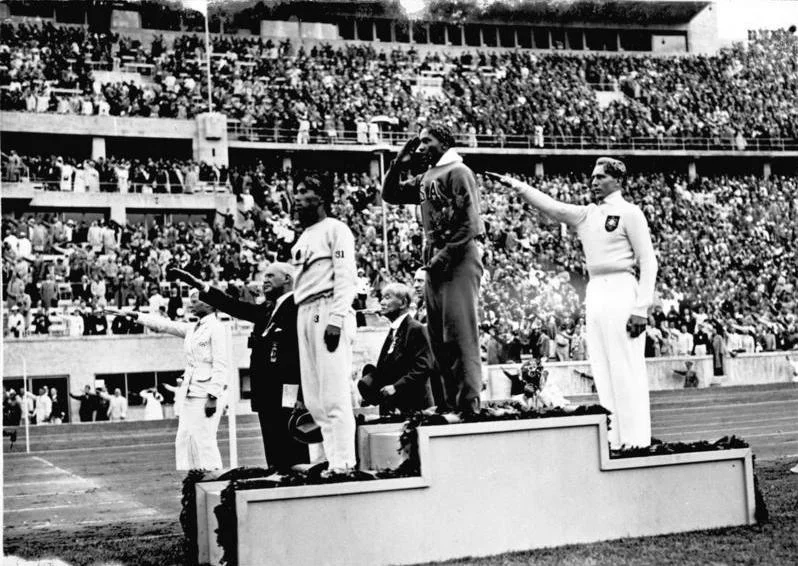 A photo of Jesse Owens standing on the medal podium with others doing the Nazi salute around him (WikiCommons). 