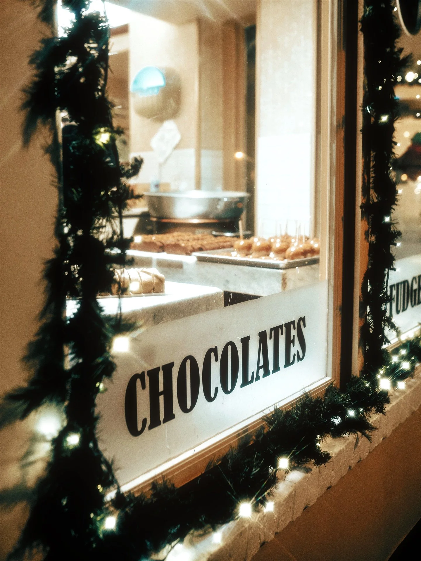 Display window with chocolates and desserts, decorated with Christmas garland and lights.