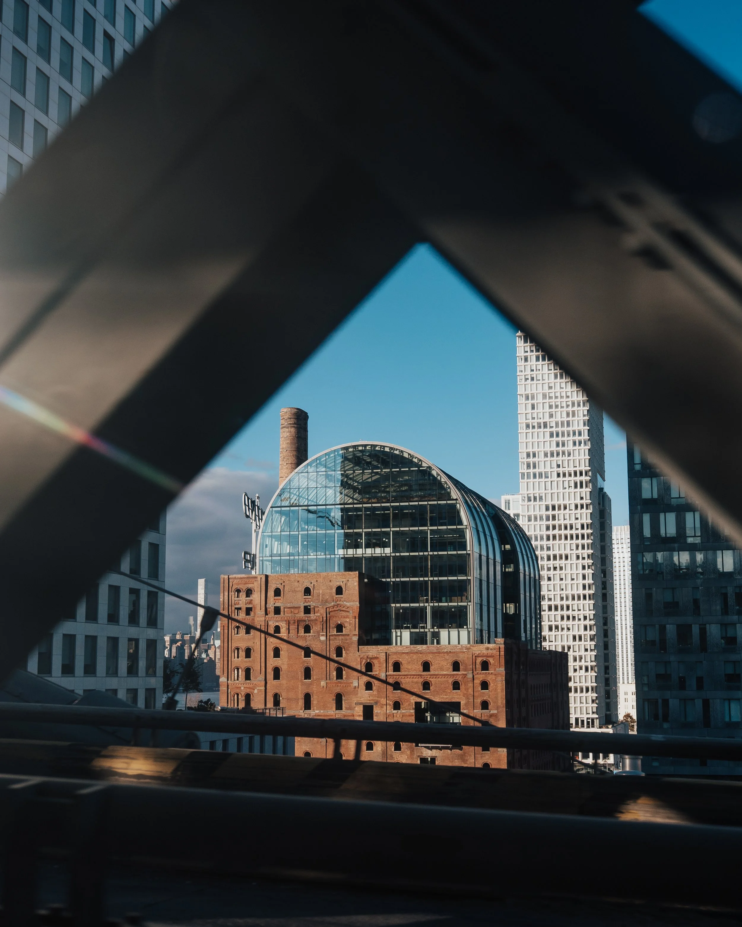 Cityscape view of modern and historic buildings through a metal railing or fence in the foreground with a blue sky.