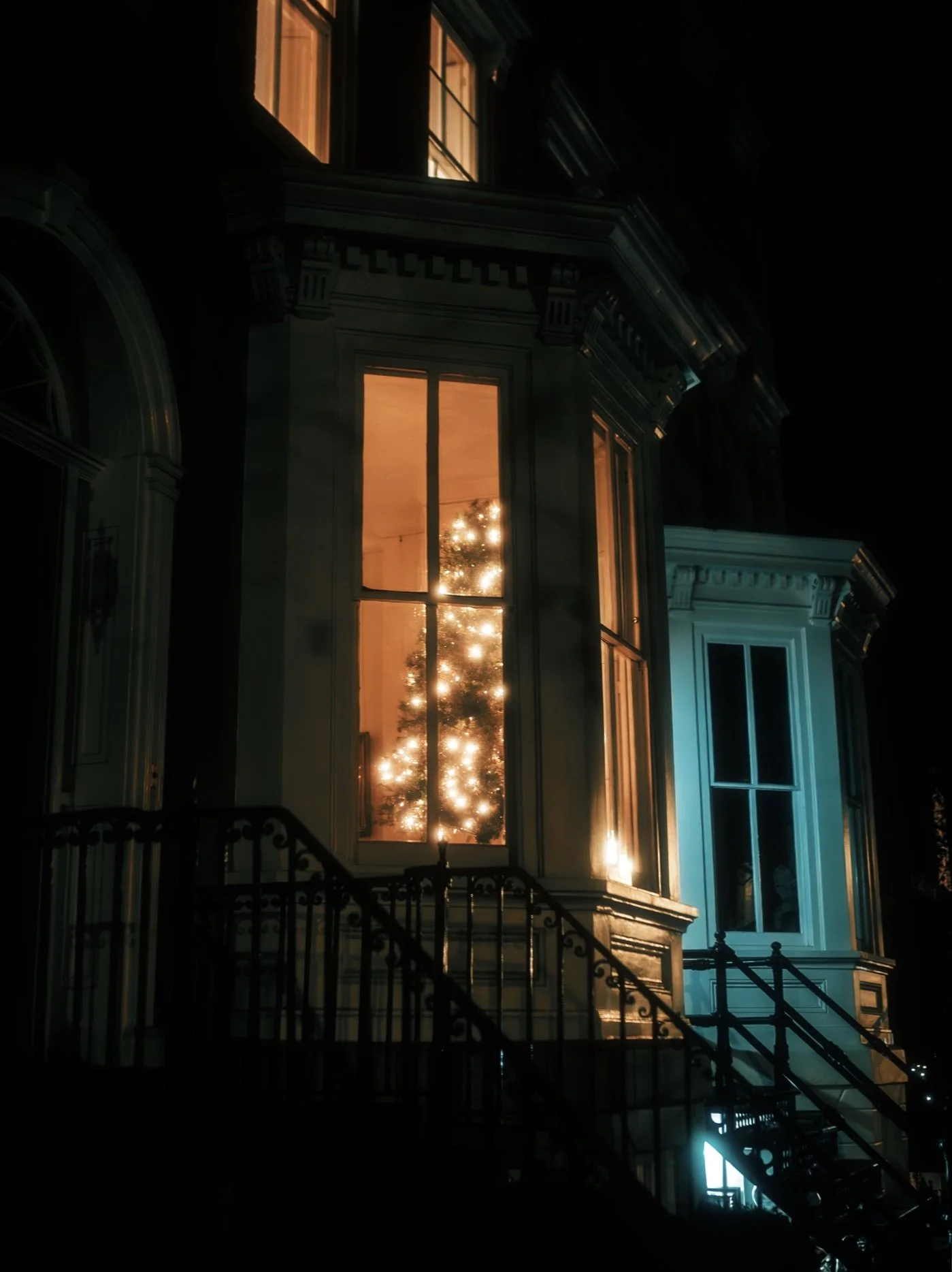 Nighttime view of a house with a Christmas tree visible through the front window, decorated with lights, and a staircase leading up to the entrance.
