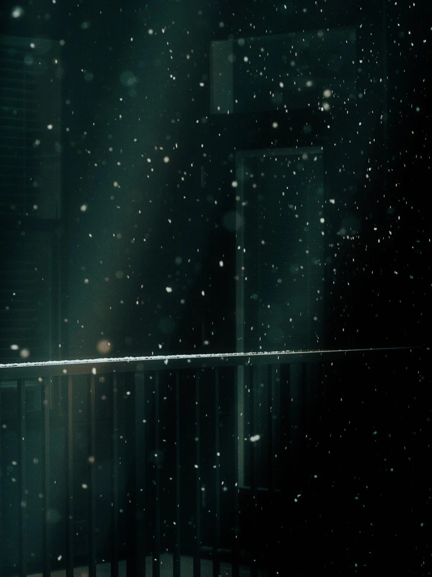 Snow falling at night on a balcony with a railing.