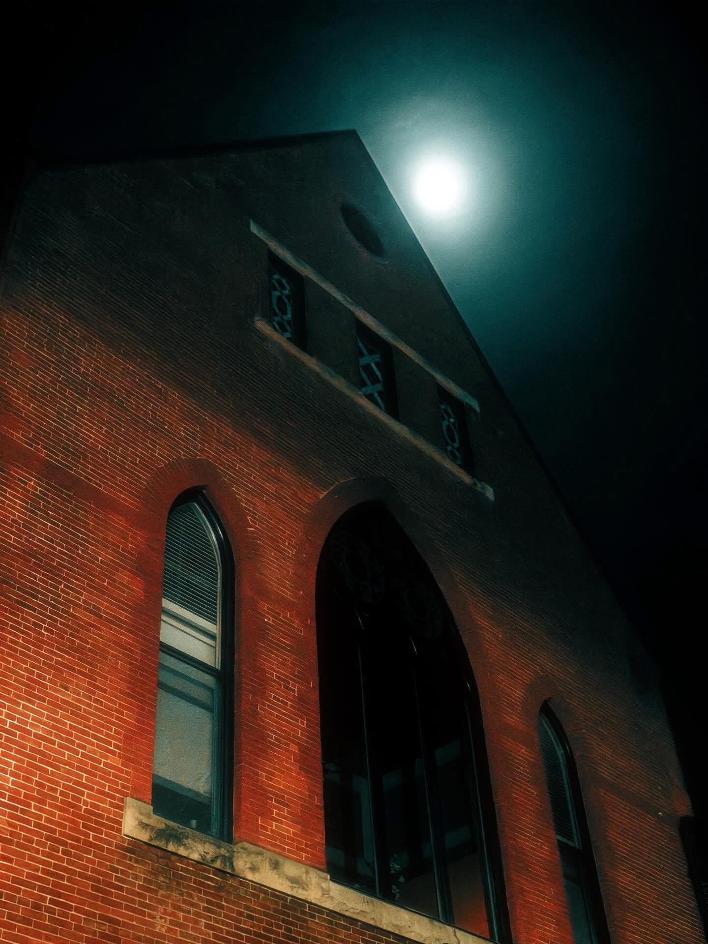 A brick building with arched windows illuminated at night under a bright full moon.