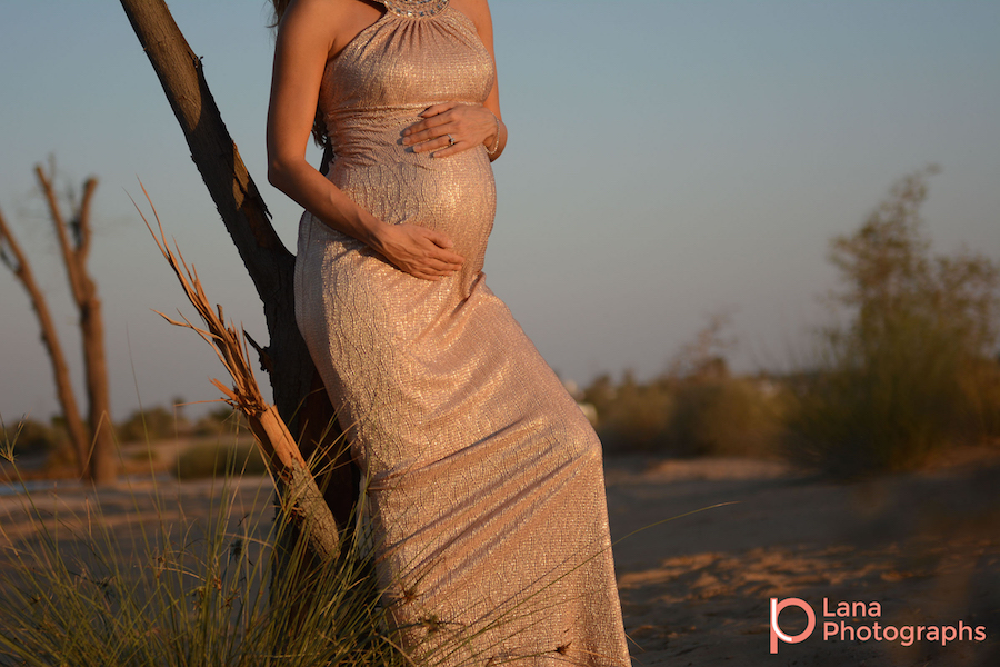 Dubai Maternity Photography portrait of pregnant woman posing against a tree in the desert as the sun sets down