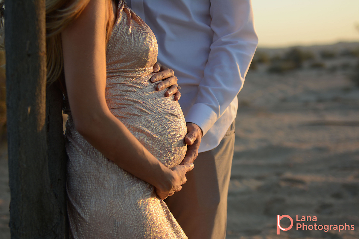 Dubai Maternity Photography portrait of expectant couple posing against a tree in the desert as the sun sets down
