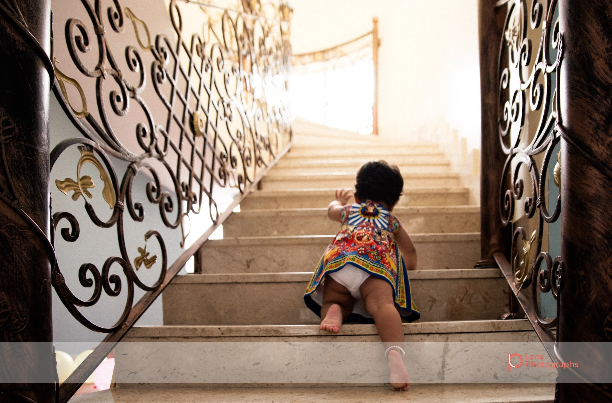 playing near a table showing a reflection of her birthday balloons little girl crawling up the stairs