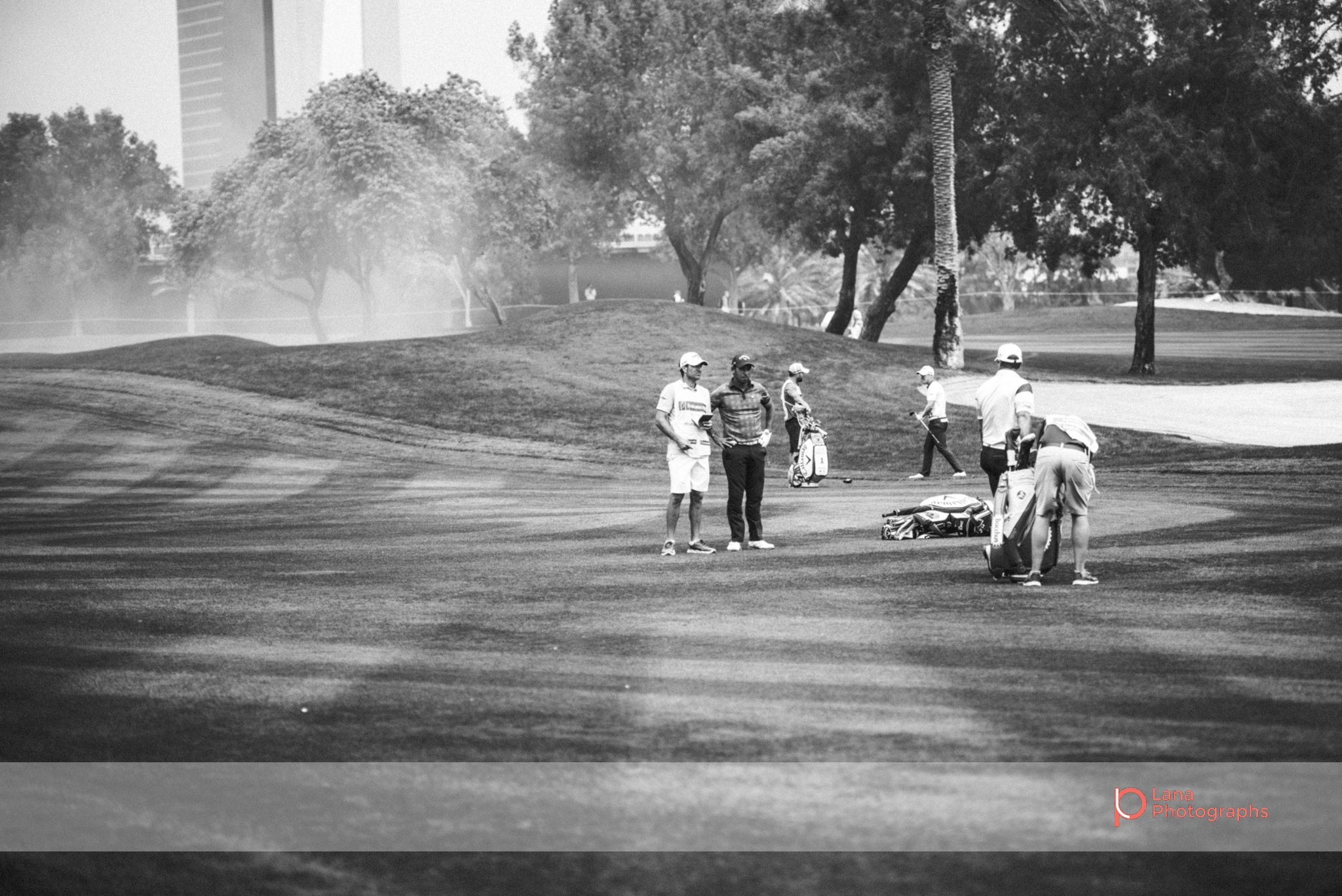 Tour players walking across the Emirates Golf Course grounds as the wind picks up behind them 