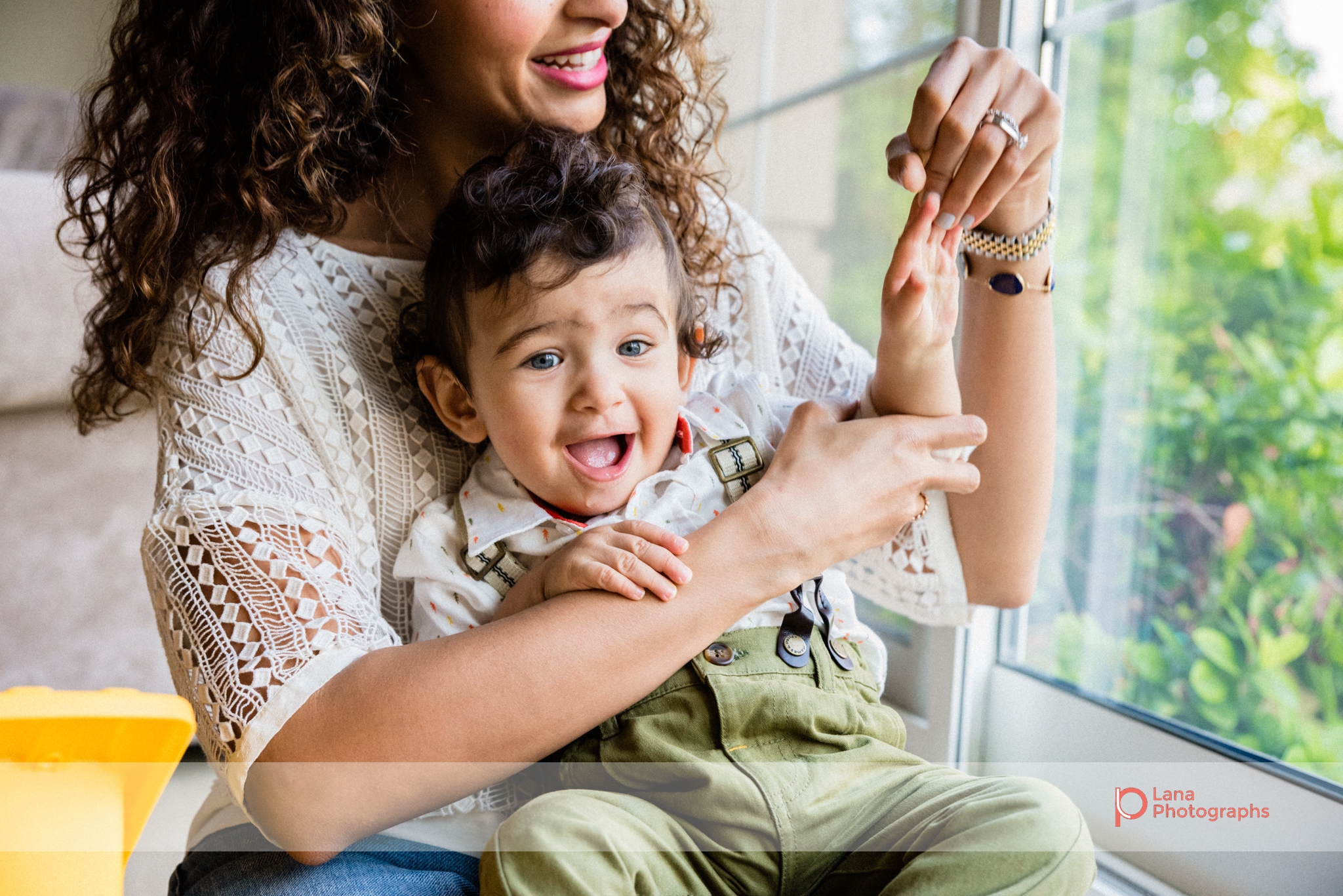 mother tickling baby as they sit together next to the window