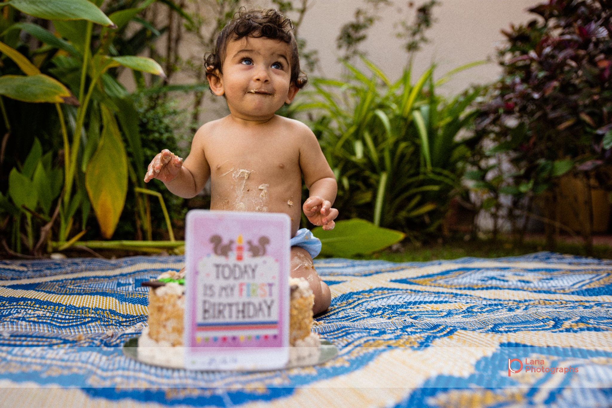 baby boy posing happily with his one year birthday cake outside his home in the garden