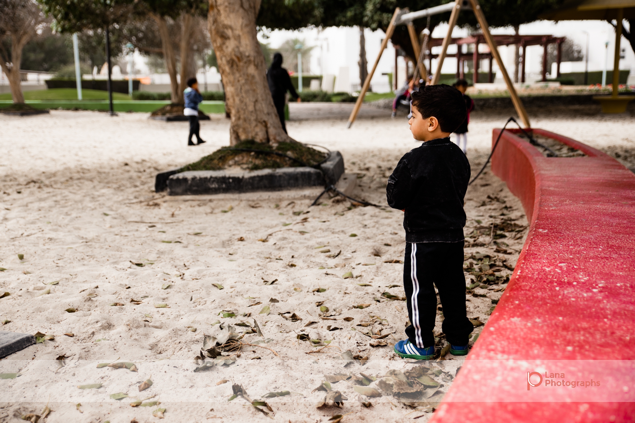 Dubai Family Photographer little boy standing in the sand by a red curb in Umm suqeim park Dubai