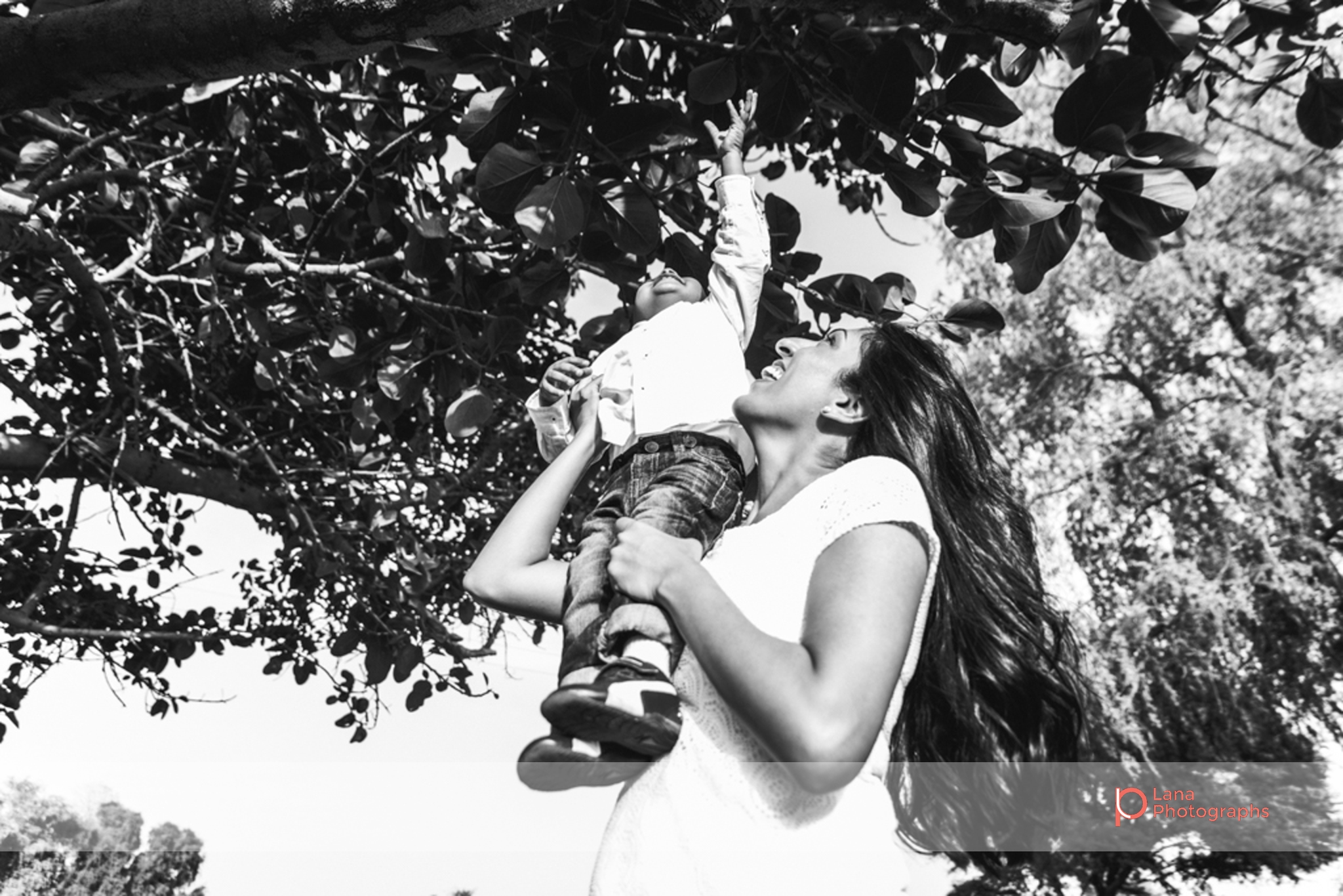 Lana Photographs Family Photographer Dubai Top Family Photographers mother with long black hair carrying her child under a tree